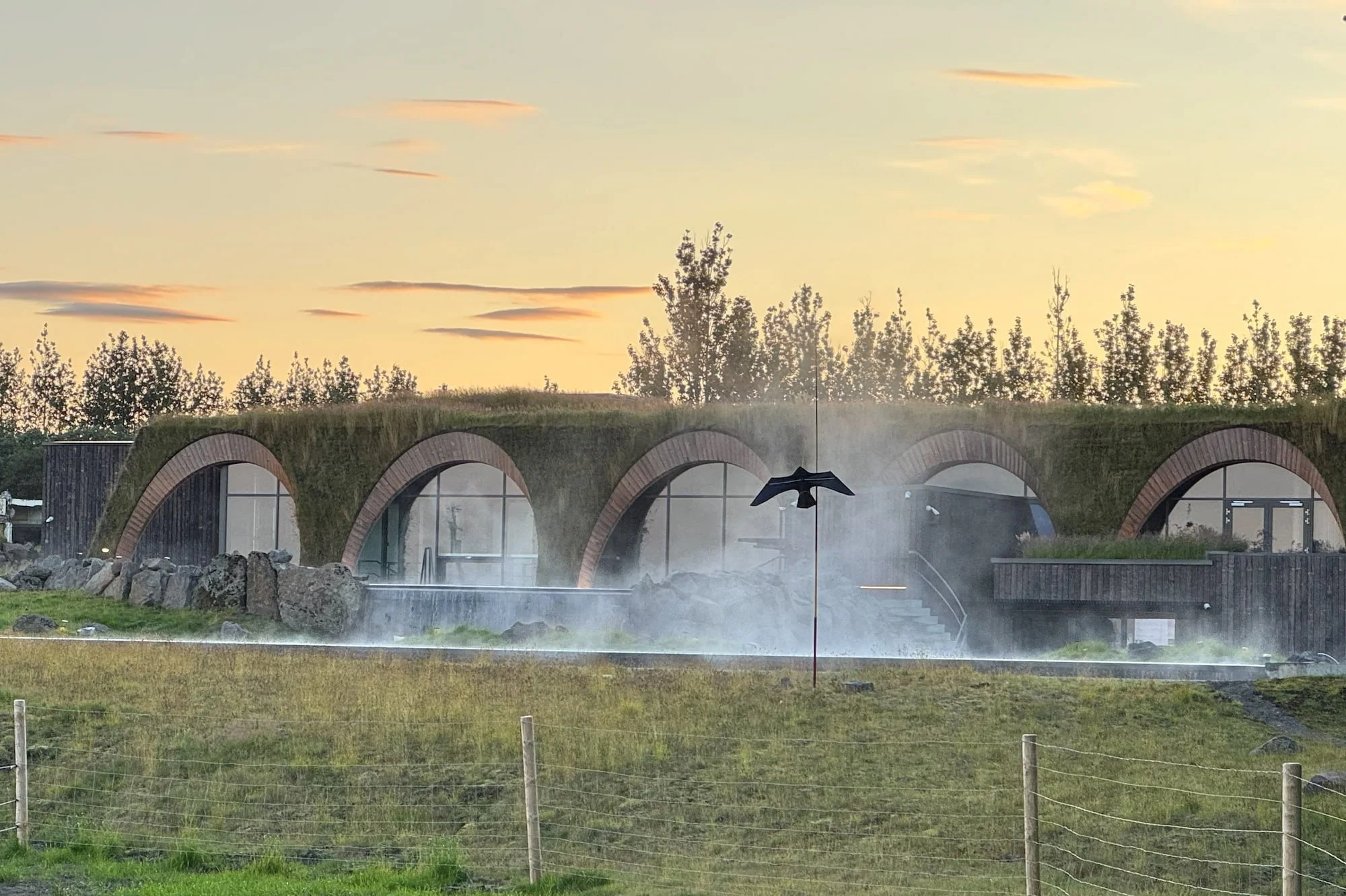 Early morning mist rising around the grass-covered roof and arched buildings of Laugarás Lagoon, Iceland.
