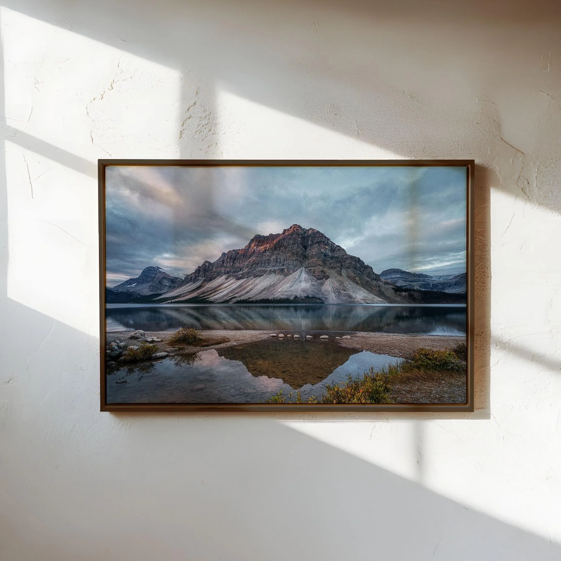 Bow Lake Reflections fine art print in a slim, dark espresso wood frame, displayed on a clean white wall with soft, natural side lighting.