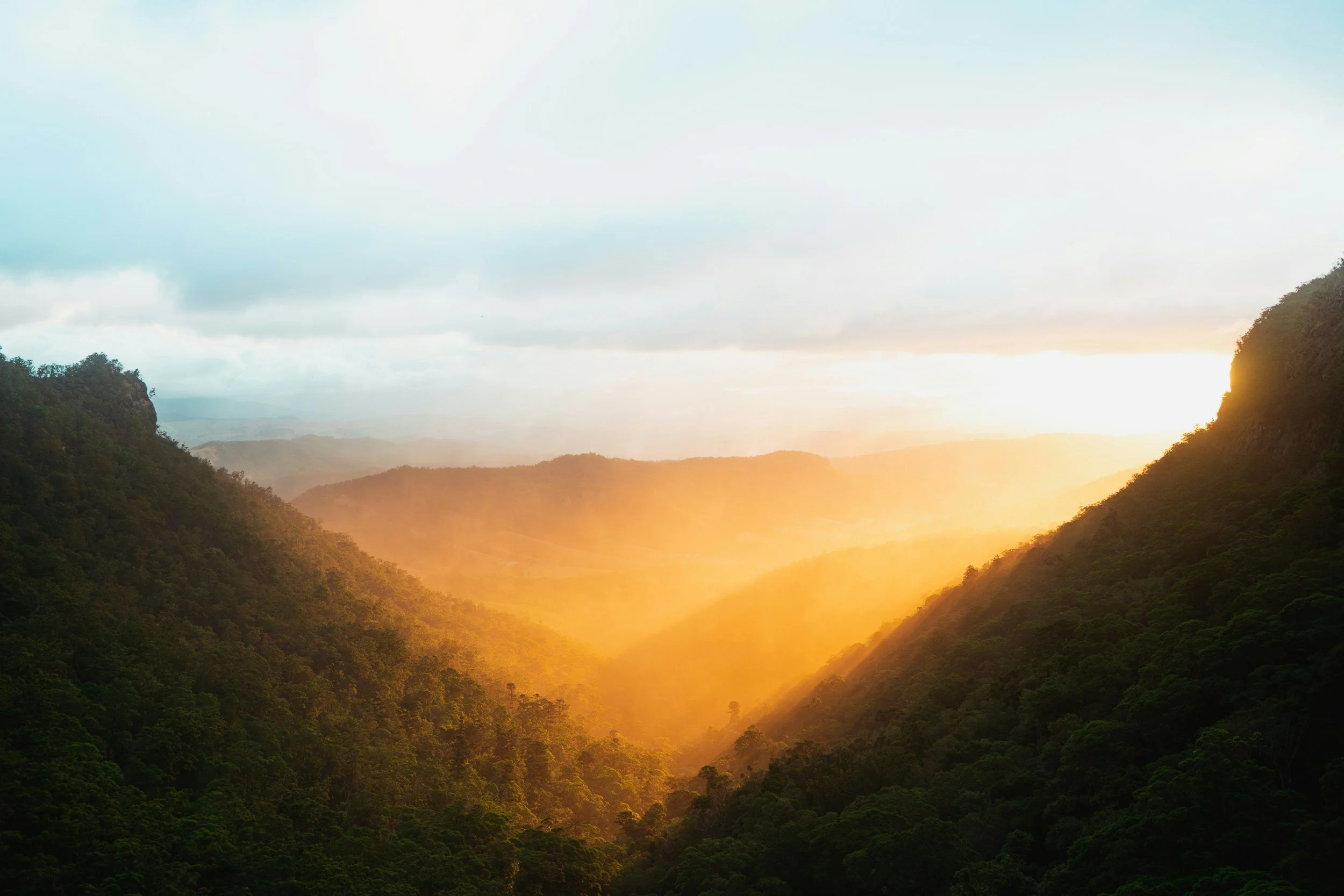 Sunset over a green mountain valley with a cloudy sky.