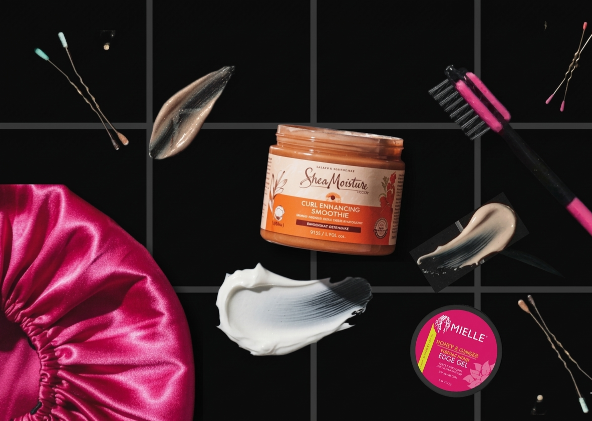 Beauty products and tools on a black background, including a pink satin bonnet, a jar of SheaMoisture Curl Enhancing Smoothie, a pink edge gel container, a facial razor, a lip gloss or serum applicator, and various swipes of facial or hair product.