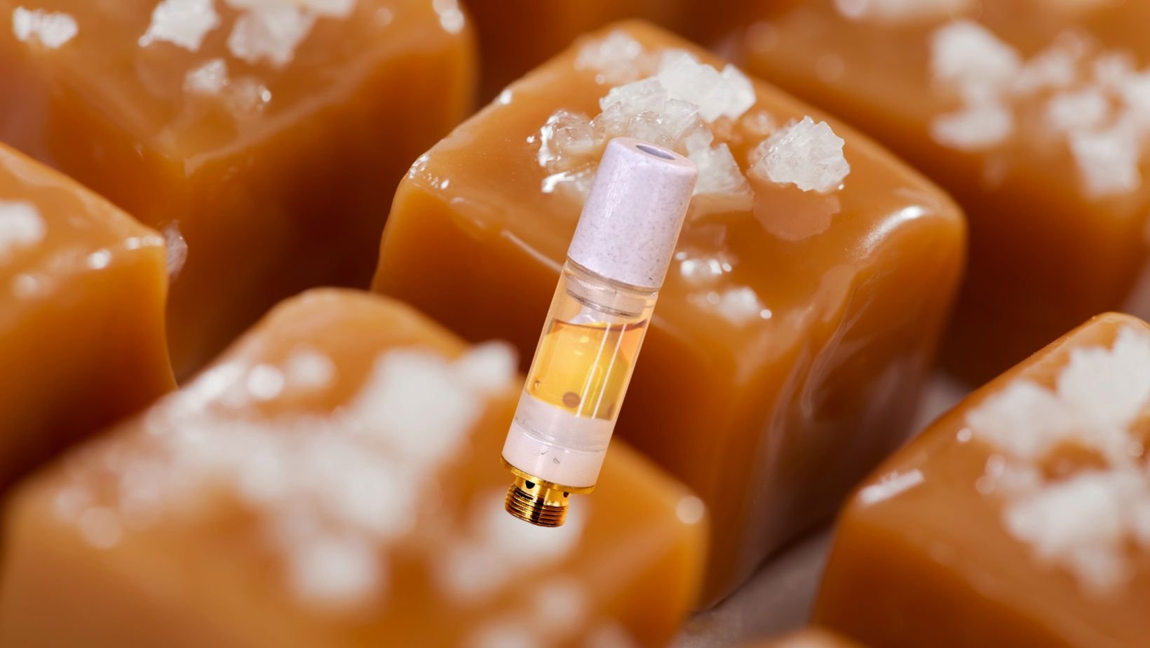 hai. live rosin cartridge with golden oil and a light-colored mouthpiece, styled against caramel-colored cubes topped with coarse salt crystals to evoke crème noir’s creamy notes and salty caramel finish.