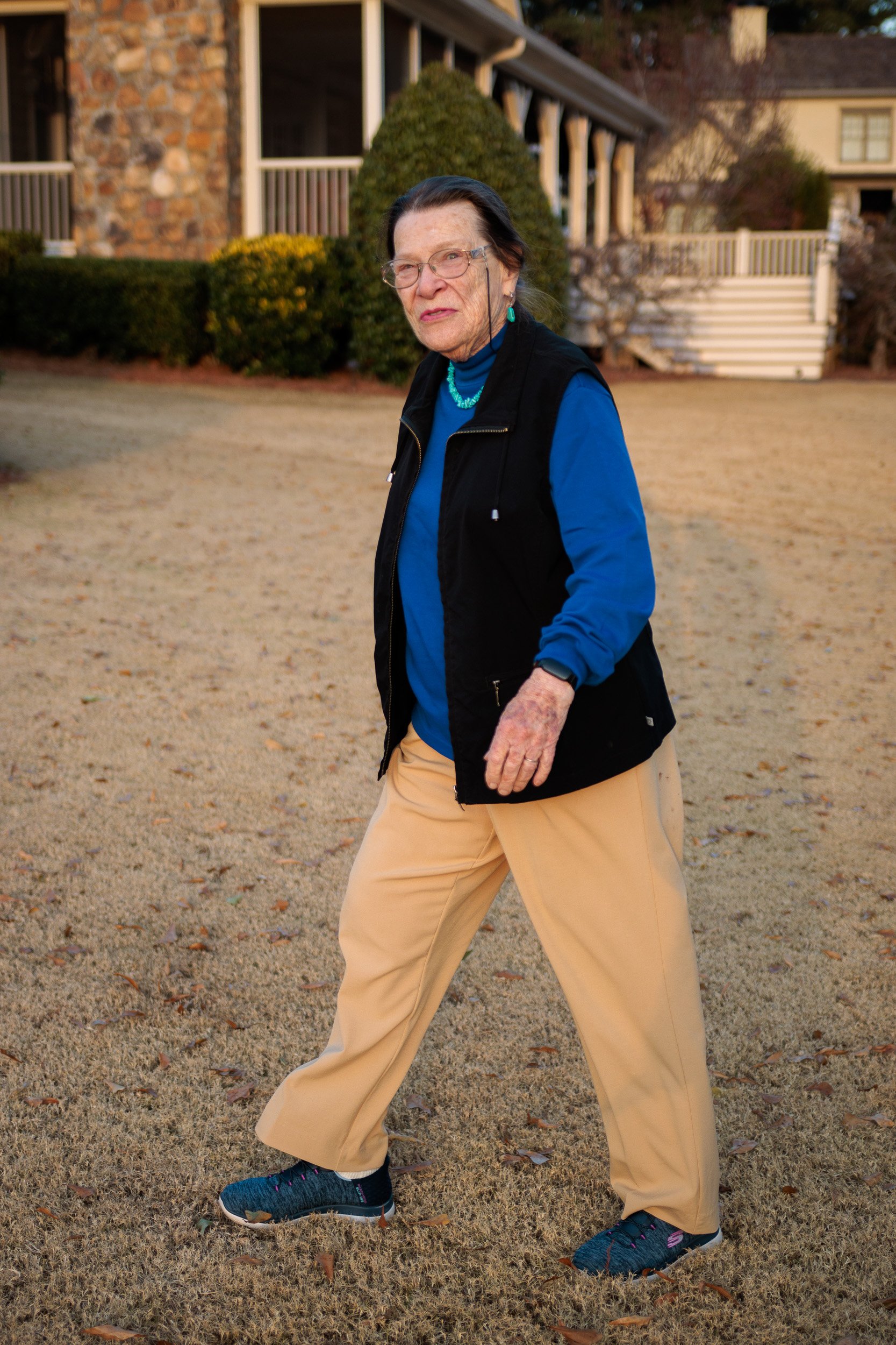 Person in a blue shirt and black vest walking across the yard
