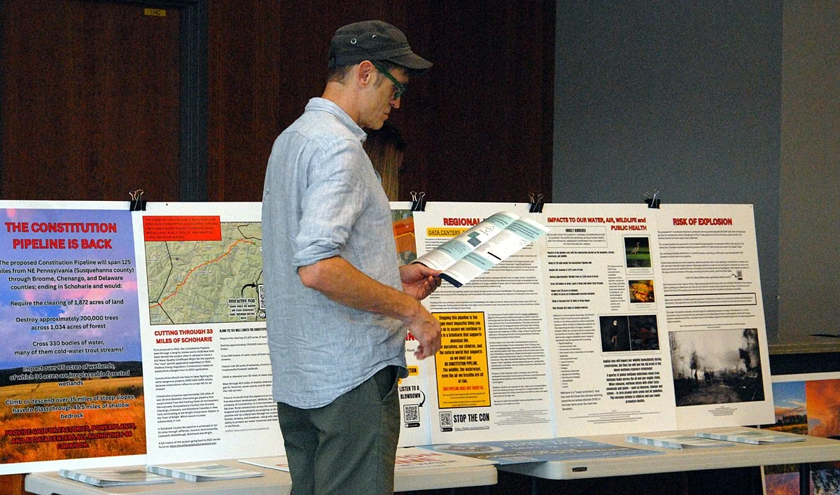 A man reads a brochhure in font of a display warning about the dangers of the proposed Constitution Pipeline.