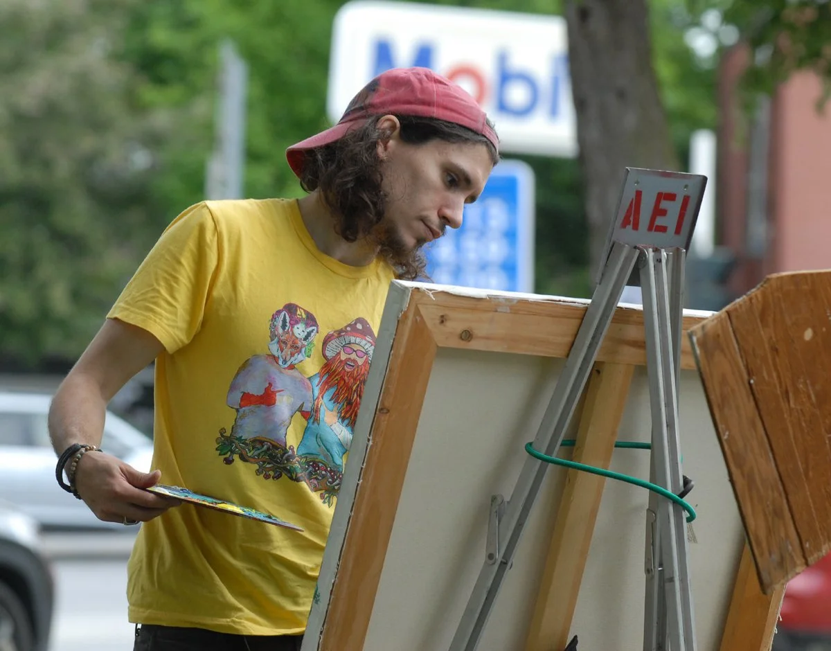 An artist in a yellow t-shirt paints in Centre Park, Cobleskill, at CPI's Arts in Action Festival.