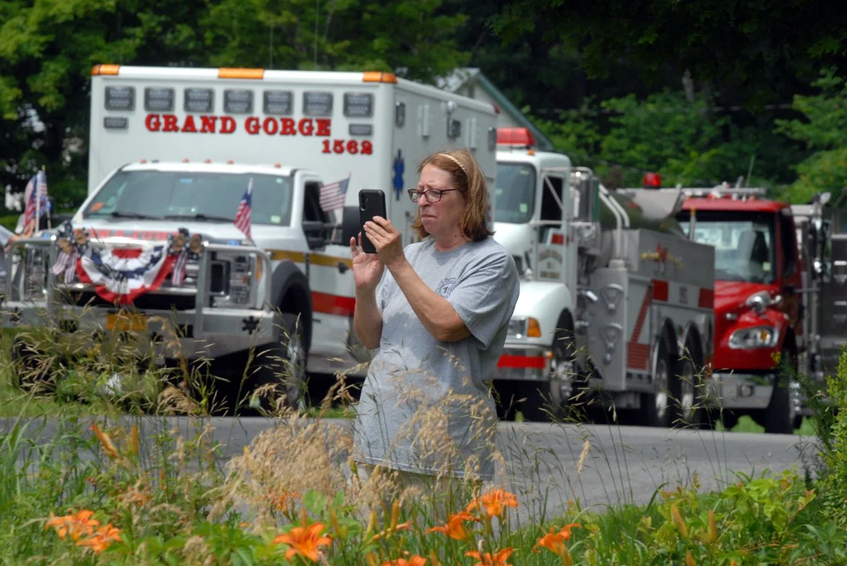 A woman uses her phone to film fire trucks before Gilboa's July 4th parade on Flat Creek Road.