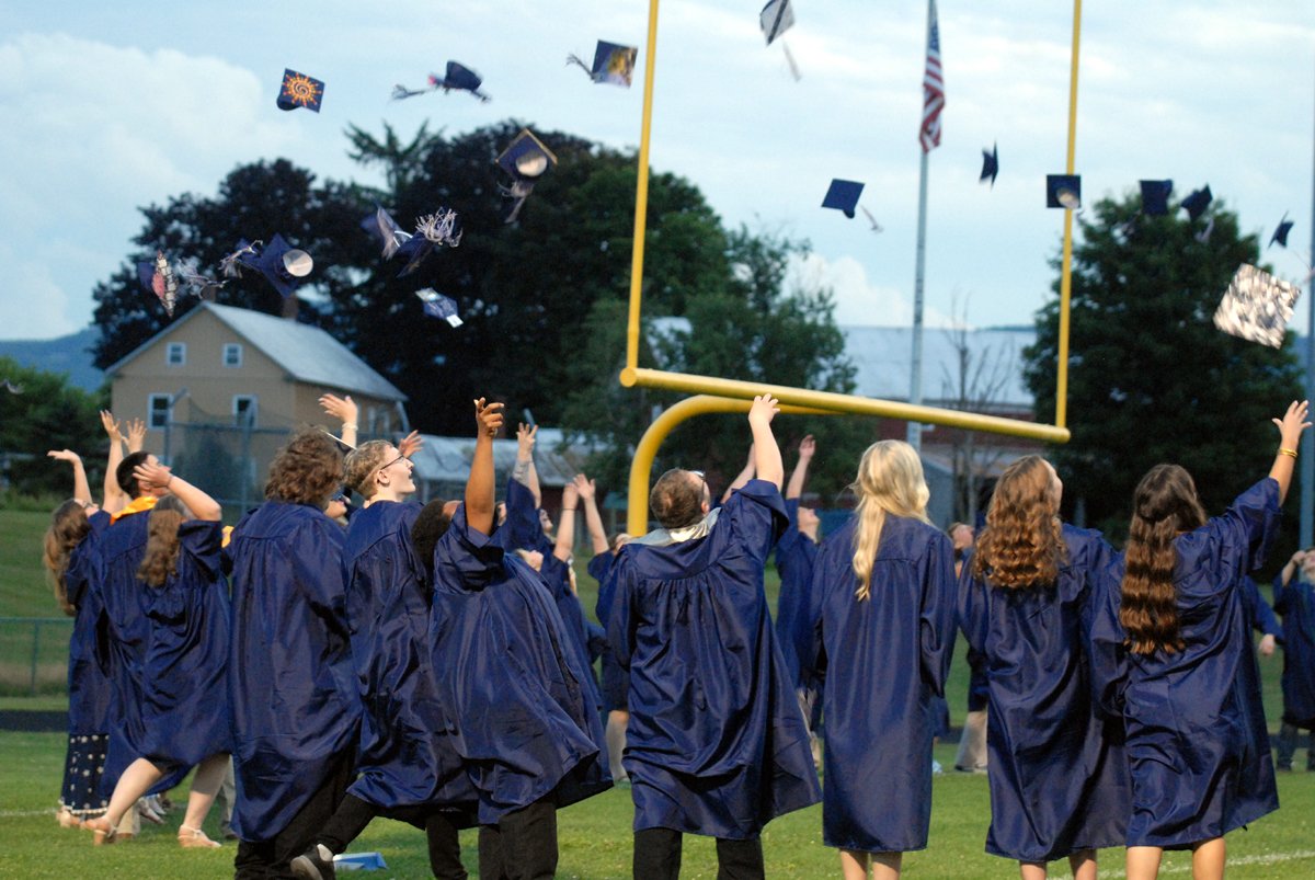 Under their football goalpost, graduates in blue robes toss their caps into the air at Cobleskill-Richmondville.