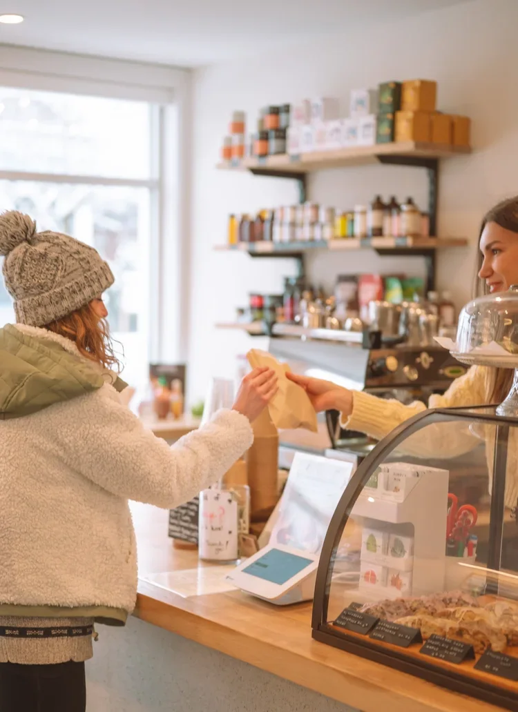 business owner at upstate ny small town coffee shop handing customer a pastry at the shop counter