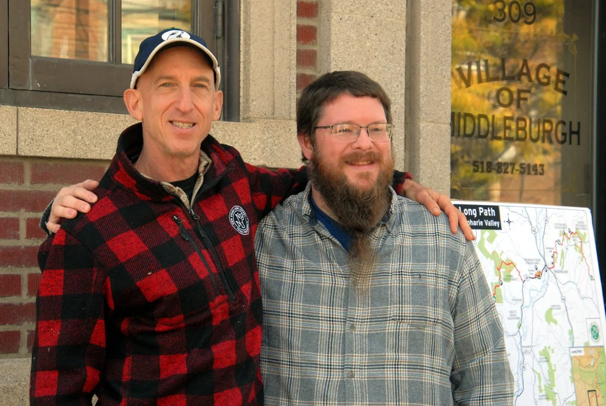 Ken Posner in red checks and Middleburgh Mayou Tim Knight stand arm in rm outside the Middleburgh Village Hall.