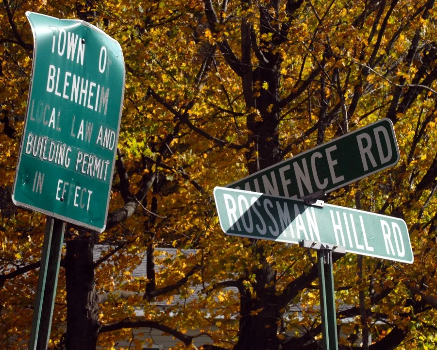 Three green road signs reading Town of Blenheim, Eminence Road, and Rossman Hil Road.