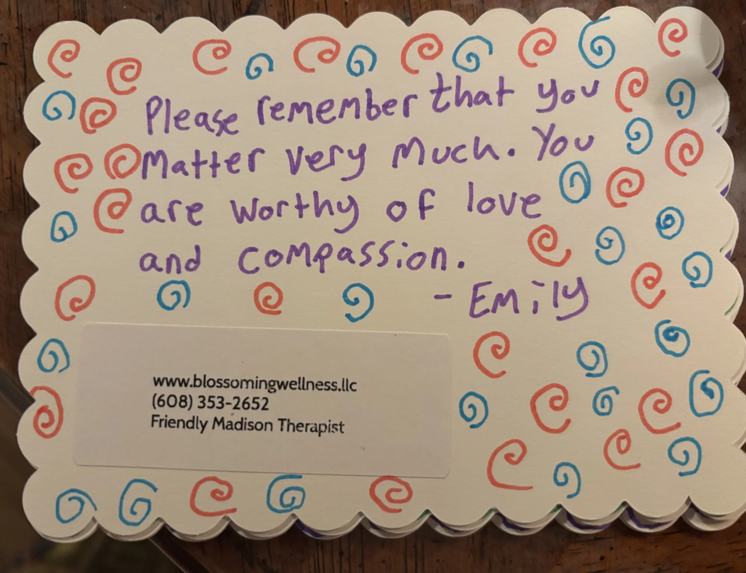 A decorative note with a scalloped edge border filled with colorful Swirl patterns and a handwritten message in purple ink that says, "Please remember that you matter very much. You are worthy of love and compassion. - Emily".