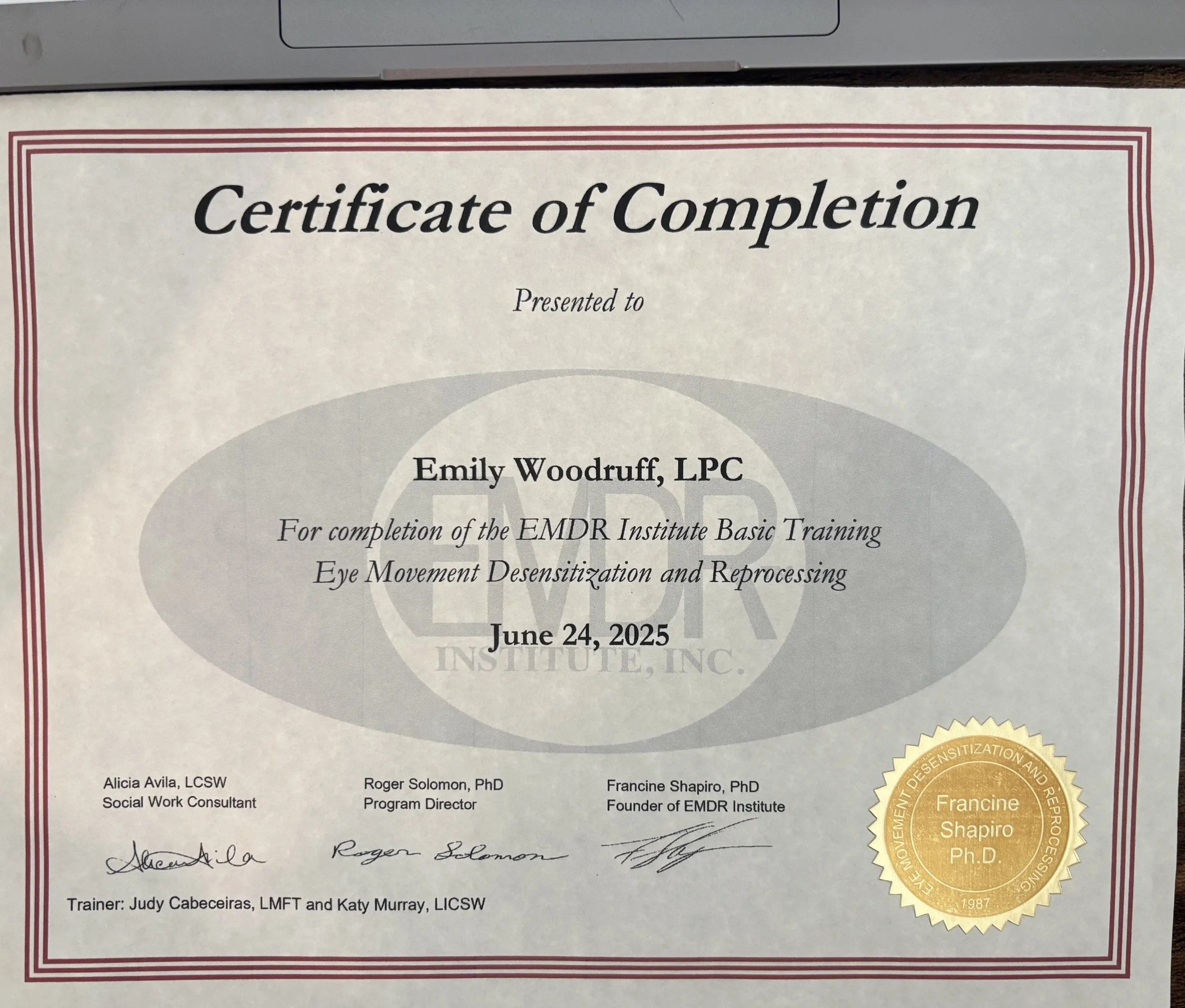 Close-up of a certificate of completion awarded to Emily Woodruff, LPC, for EMDR Institute Basic Training, dated June 24, 2025, with signatures and gold embossed seal.