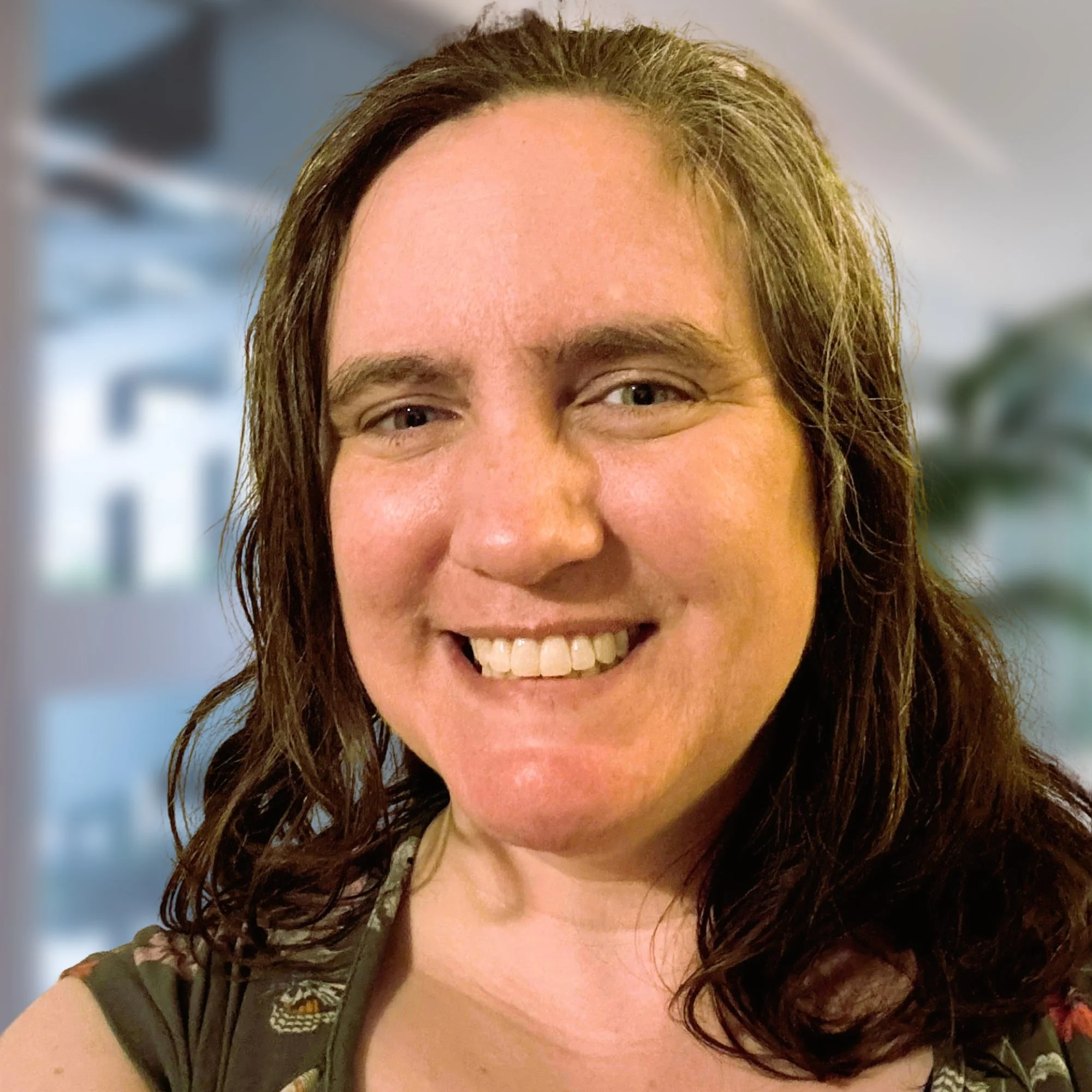 Close-up of a woman with light brown, curly hair smiling at the camera, with a blurred background.