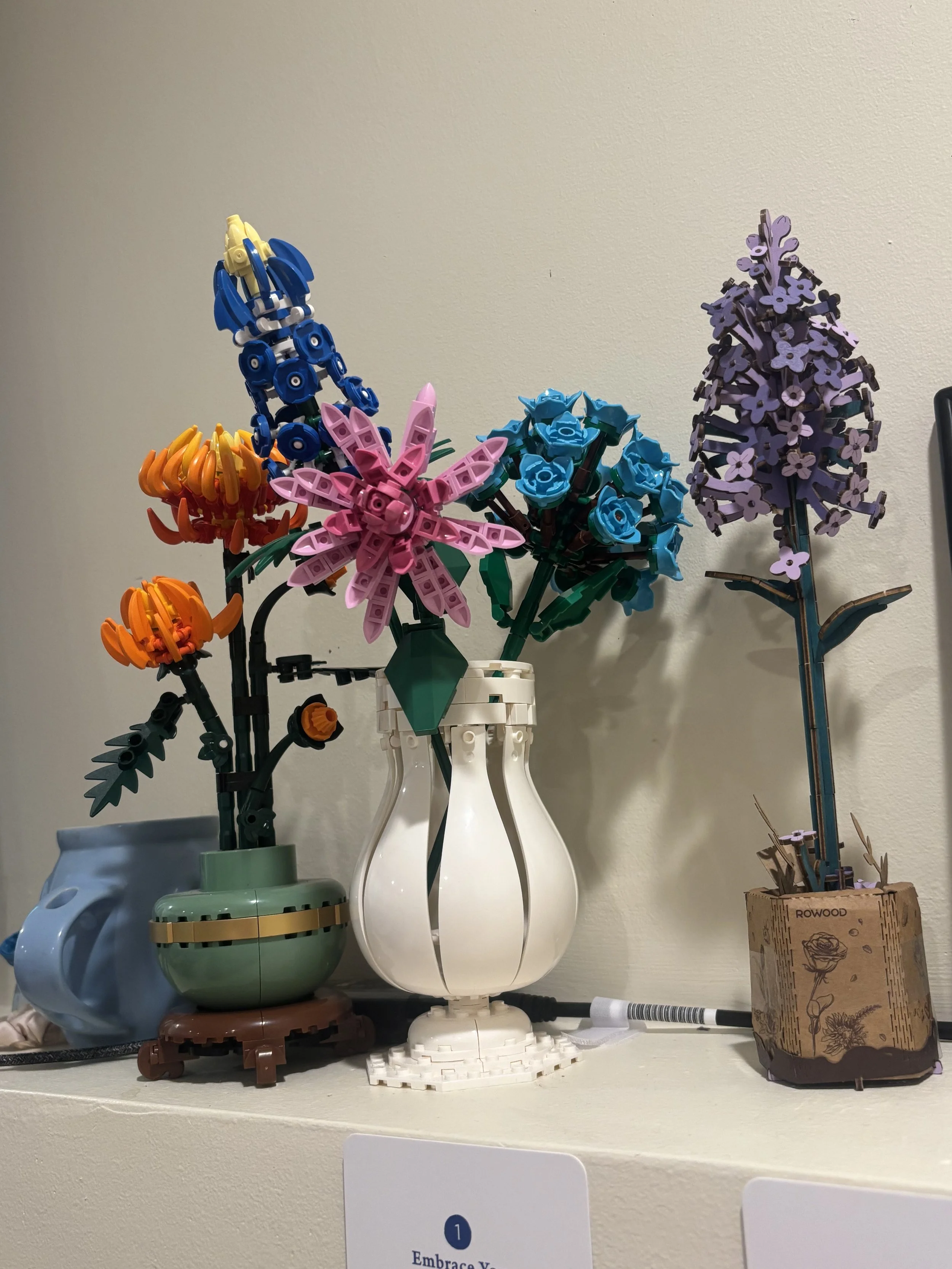 Arranged colorful artificial flowers on a shelf with various containers and a marker pen in virtual EMDR therapy office.