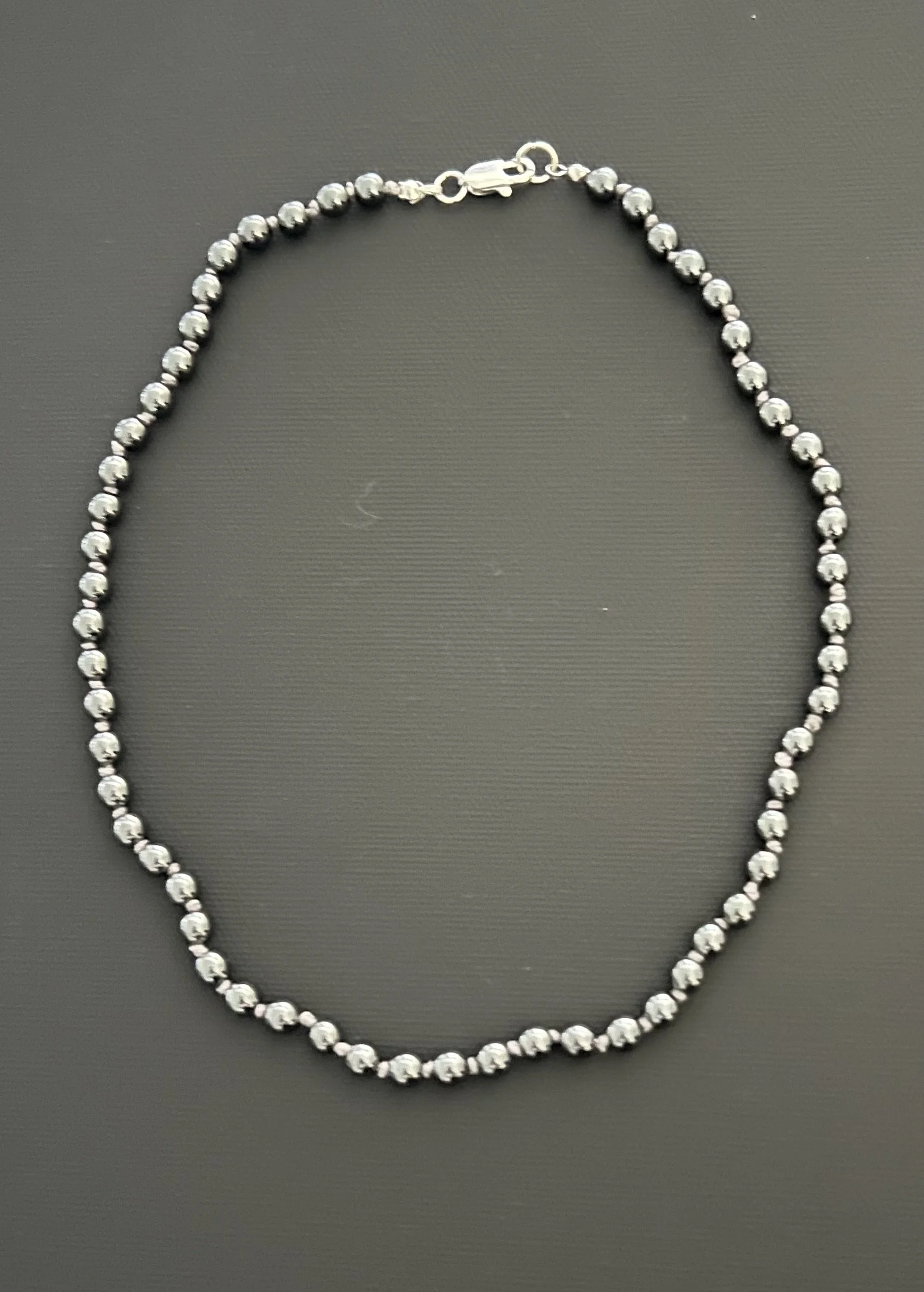 17 inch silvery black hemitite beads handknotted with back clasp. Similar to a traditional string of pearls