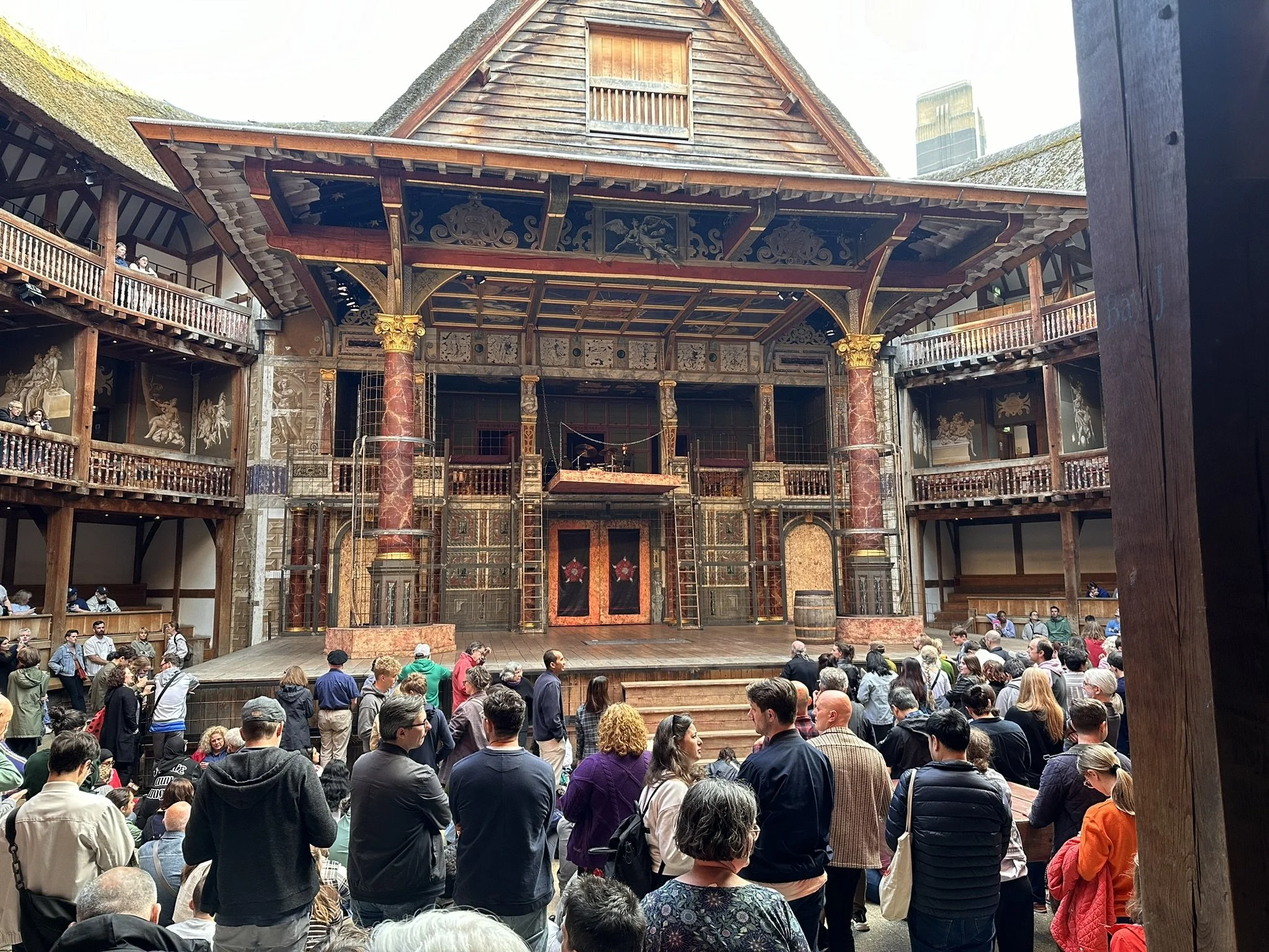 Crowd gathered in front of a theater stage with elaborate wooden and painted decorations, featuring a maroon and gold color scheme.