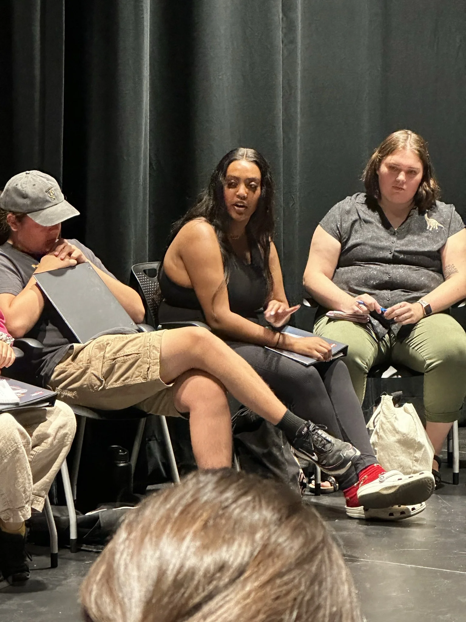 Three women sitting on chairs in front of a dark curtain, engaged in a discussion or panel.