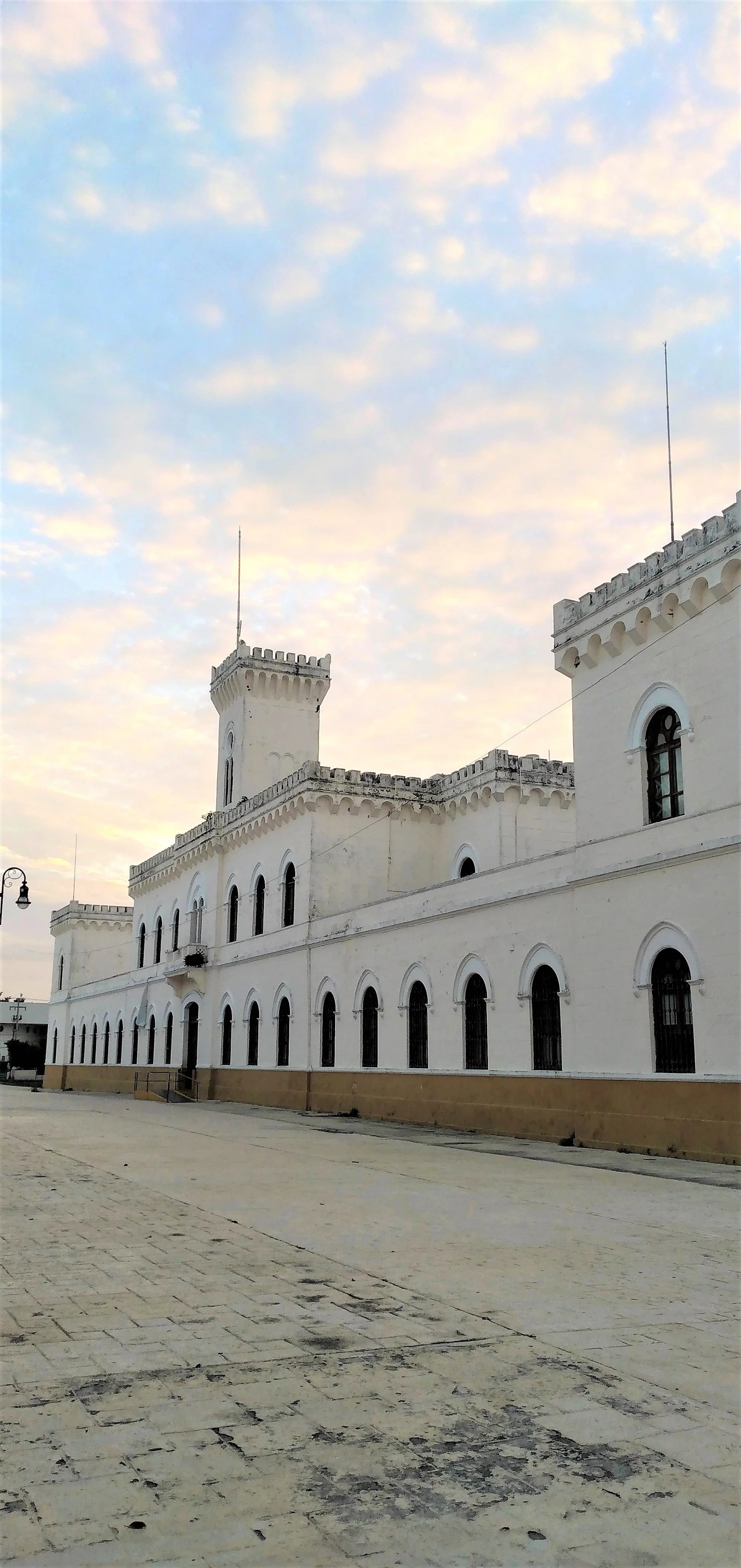 A white castle with rounded arched windows and battlements under a sky with scattered clouds.