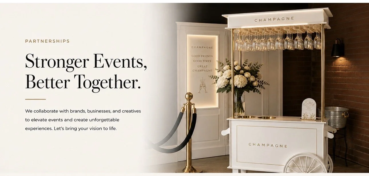 A champagne cart with hanging glasses, a floral arrangement, and decorative signs, set against a wall with a brick section and warm lighting.