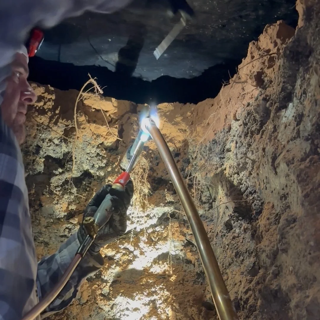 Master Plumber Nick Green silver-soldering a copper water line inside an excavated tunnel beneath a hom