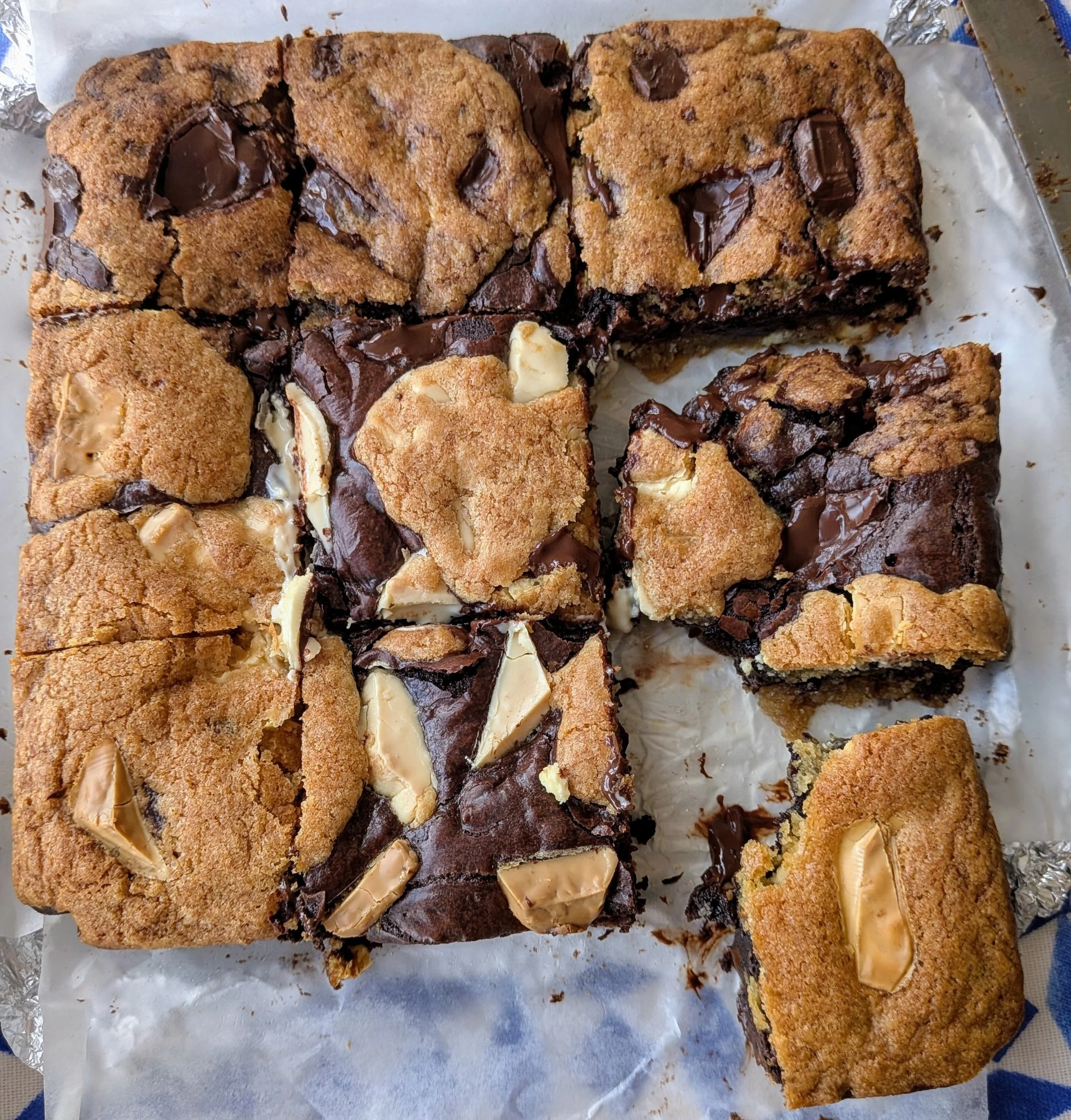 A tray of assorted brownies with some topped with white chocolate pieces and others with dark chocolate chunks, cut into squares.