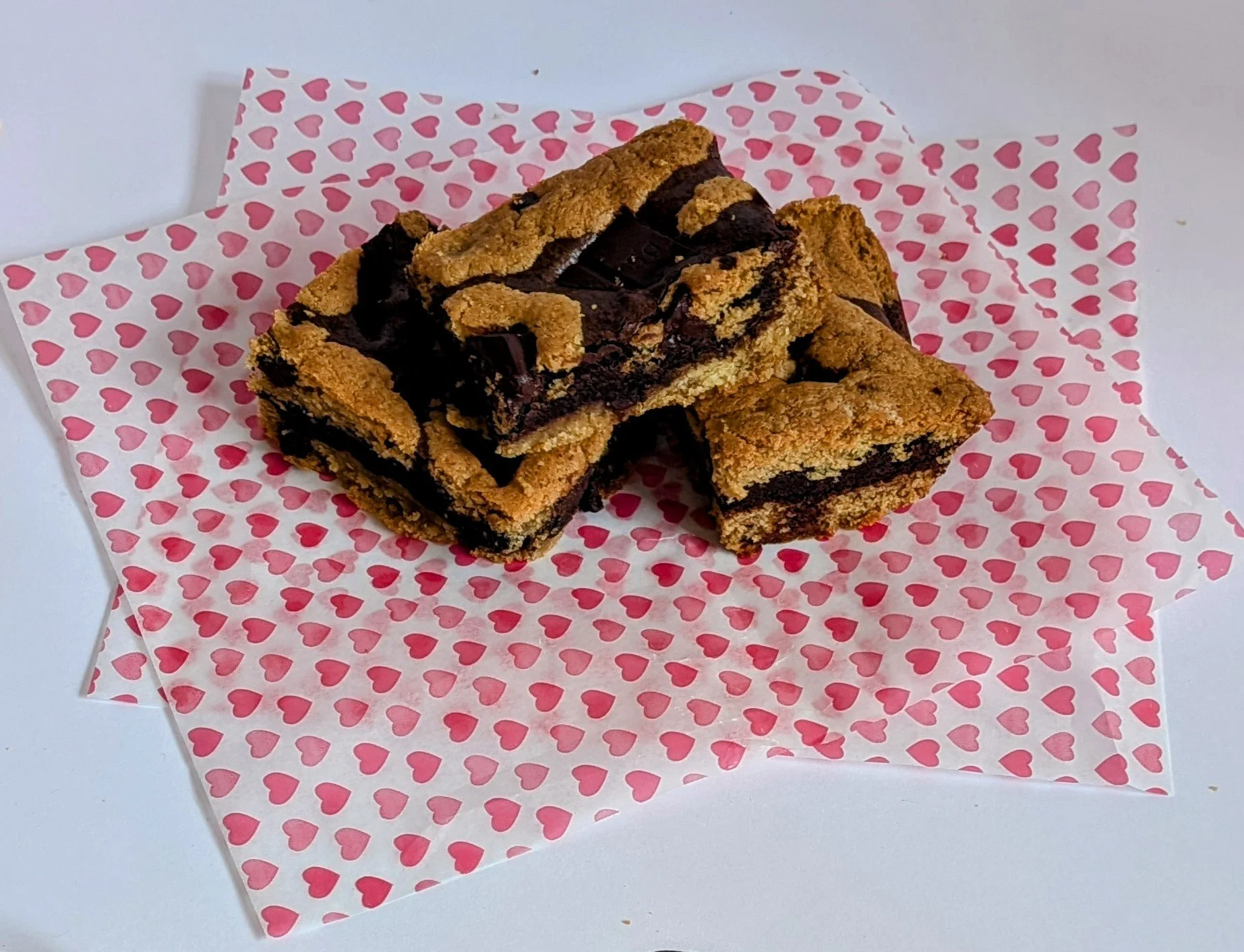Three double chocolate chip cookie bars on pink paper with red heart pattern.