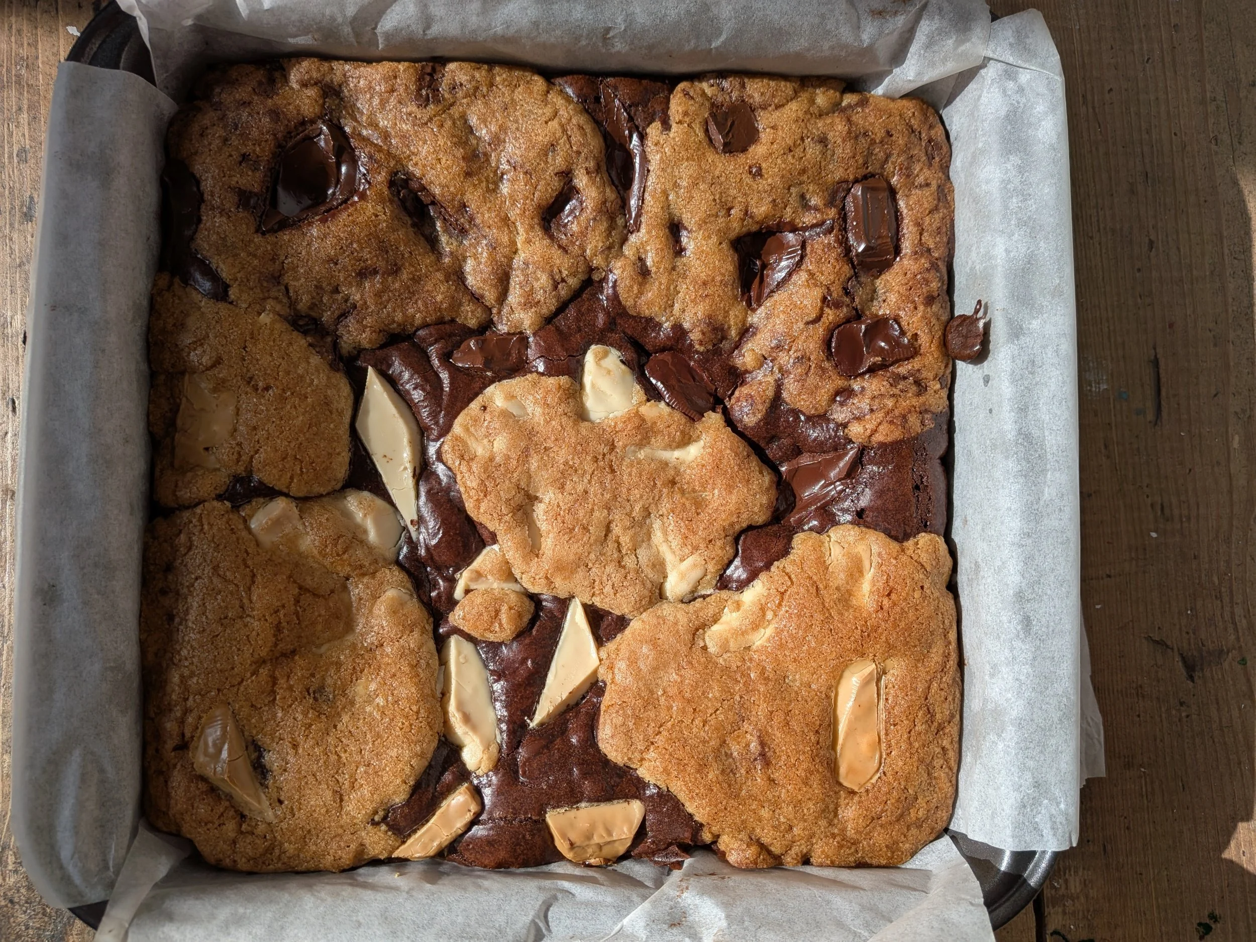 A baking tray with six large chocolate chip cookies and three white chocolate chunk cookies on parchment paper.