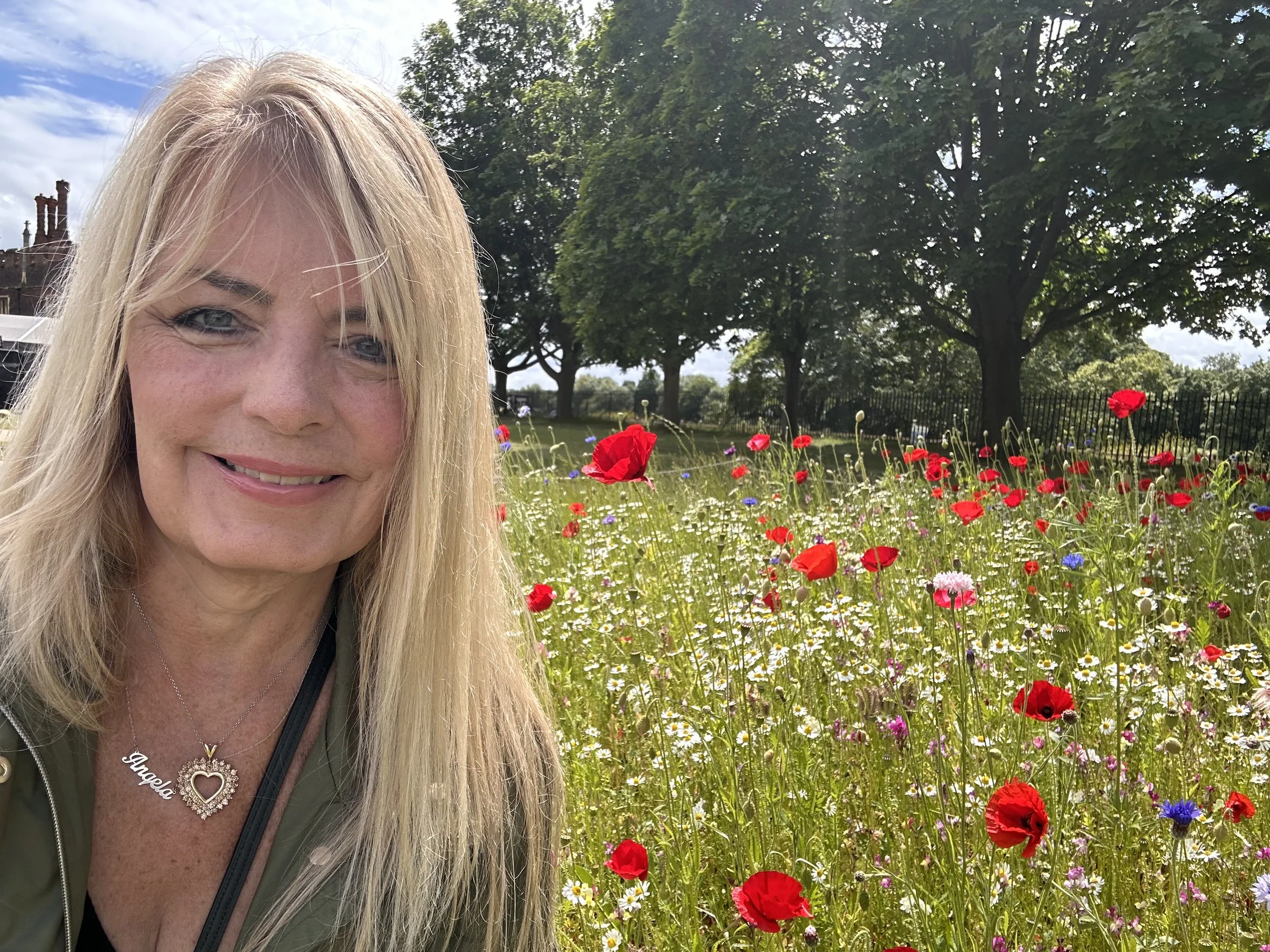 Angela standing at Hampton Court Palace with red poppies in the background, reflecting on historic grounds during a quiet moment of travel in England.
