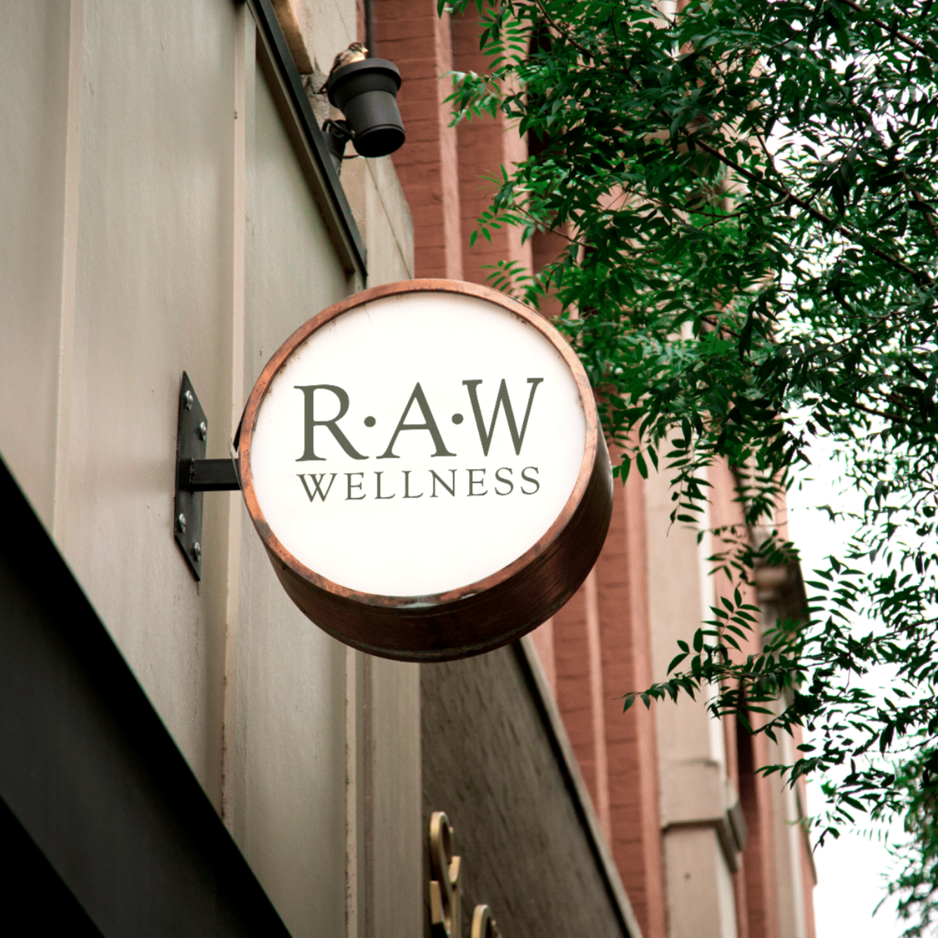 A circular sign on a building reads "RAW WELLNESS" with trees partially covering the facade.