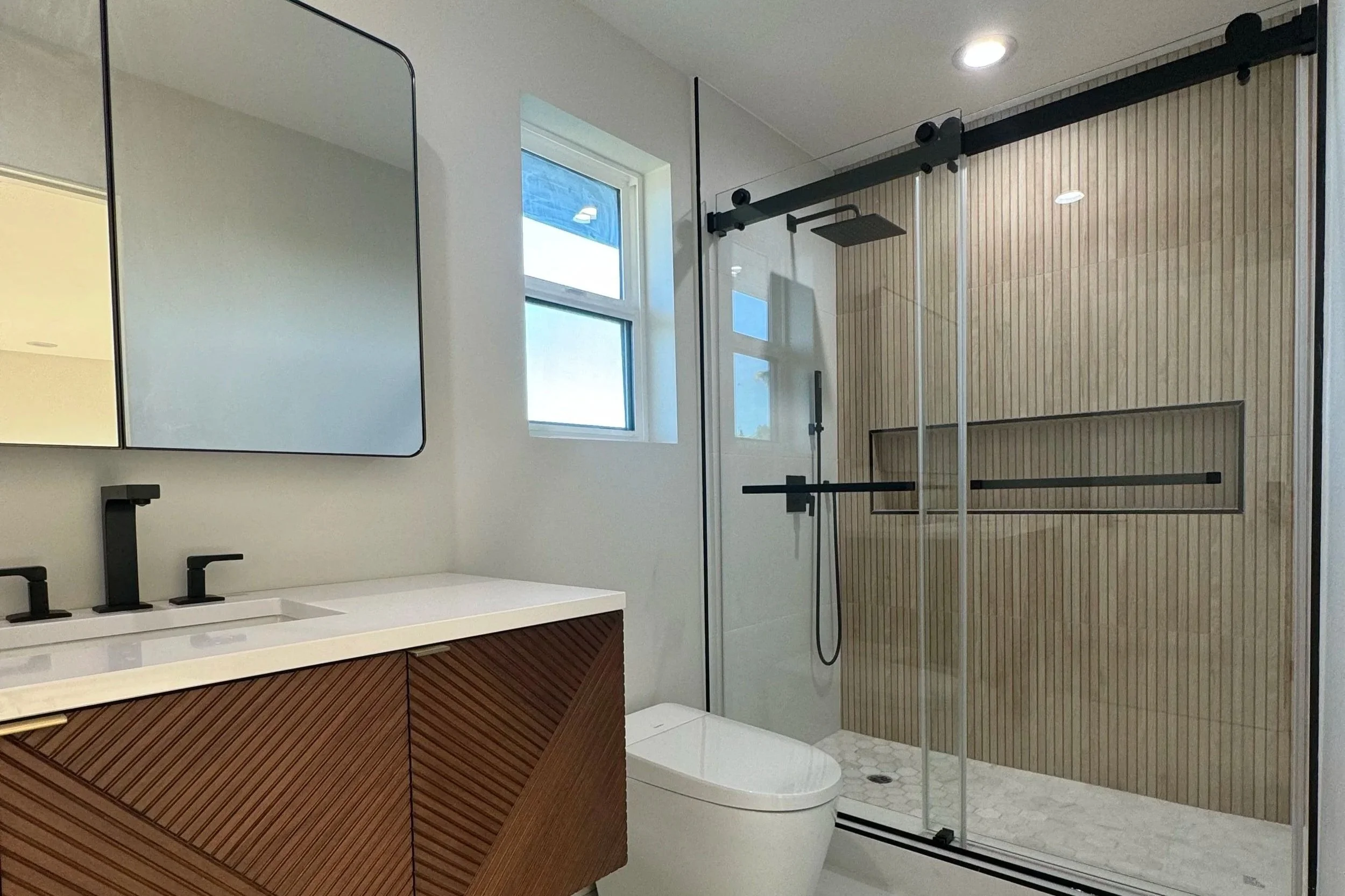 Modern bathroom with a glass shower enclosure, a white vanity with black fixtures, a mirror, and a window with natural light.