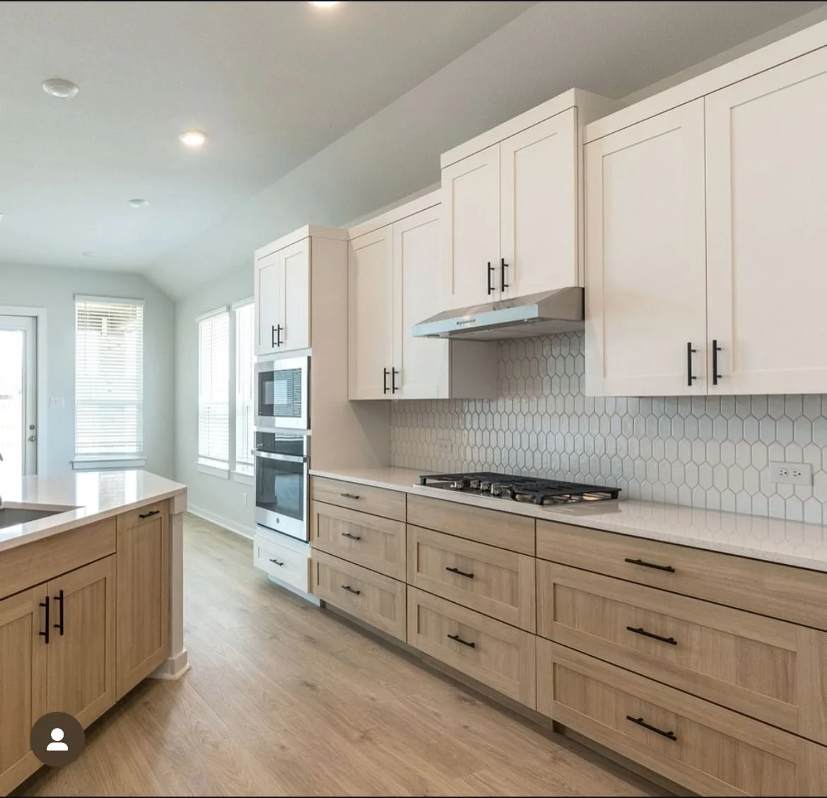 Modern kitchen with light wood cabinets, white countertops, stainless steel oven and microwave, hexagon tile backsplash, and wood flooring.