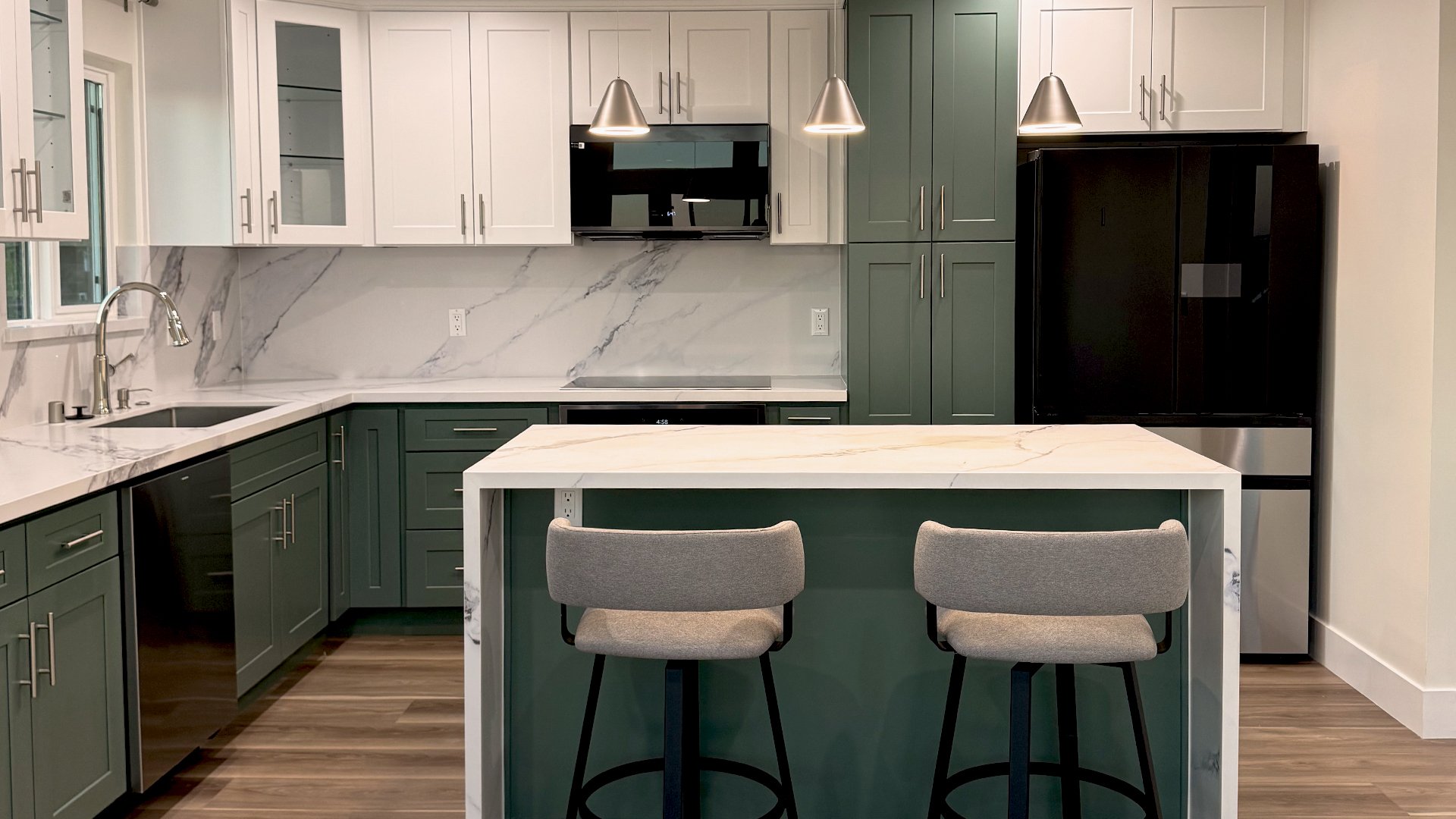 Modern kitchen with green and white cabinets, marble backsplash and countertops, black refrigerator, built-in microwave, and two gray bar stools at a white marble island.