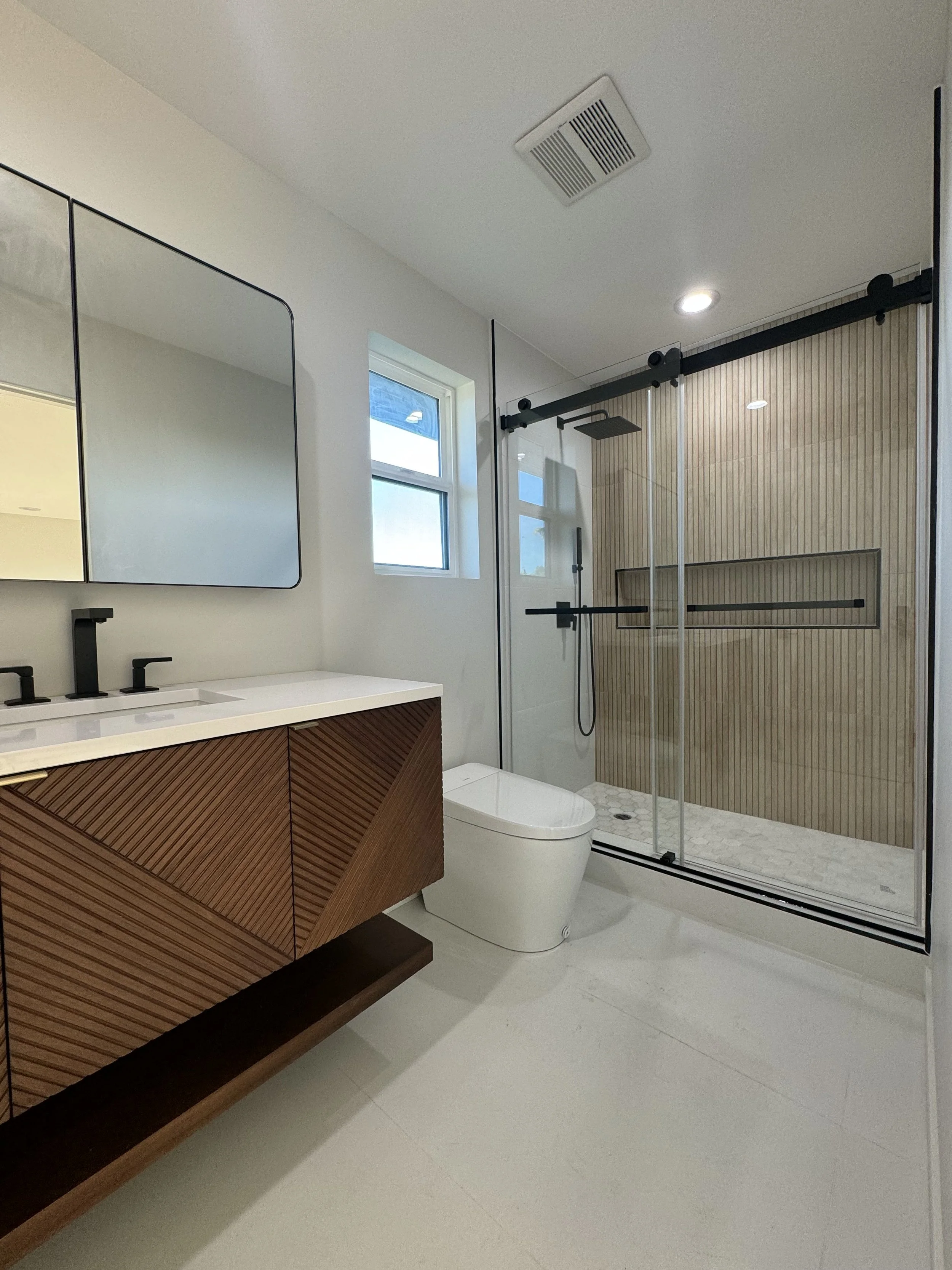 Modern bathroom with a wooden vanity, white countertop, black fixtures, a white toilet, and a glass shower with a wooden accent wall and sliding door.