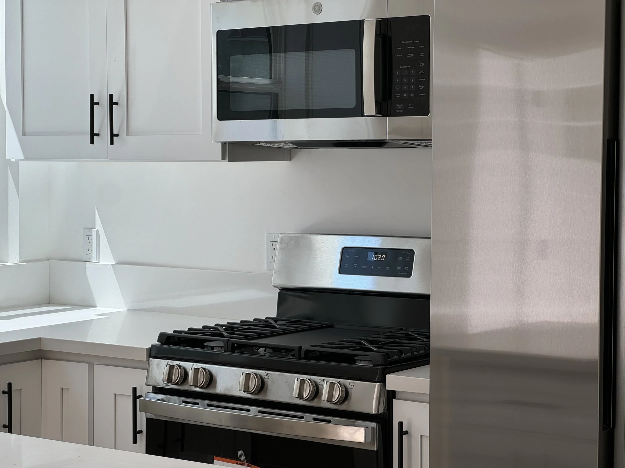 Modern kitchen with white cabinets, stainless steel microwave, oven, and refrigerator.