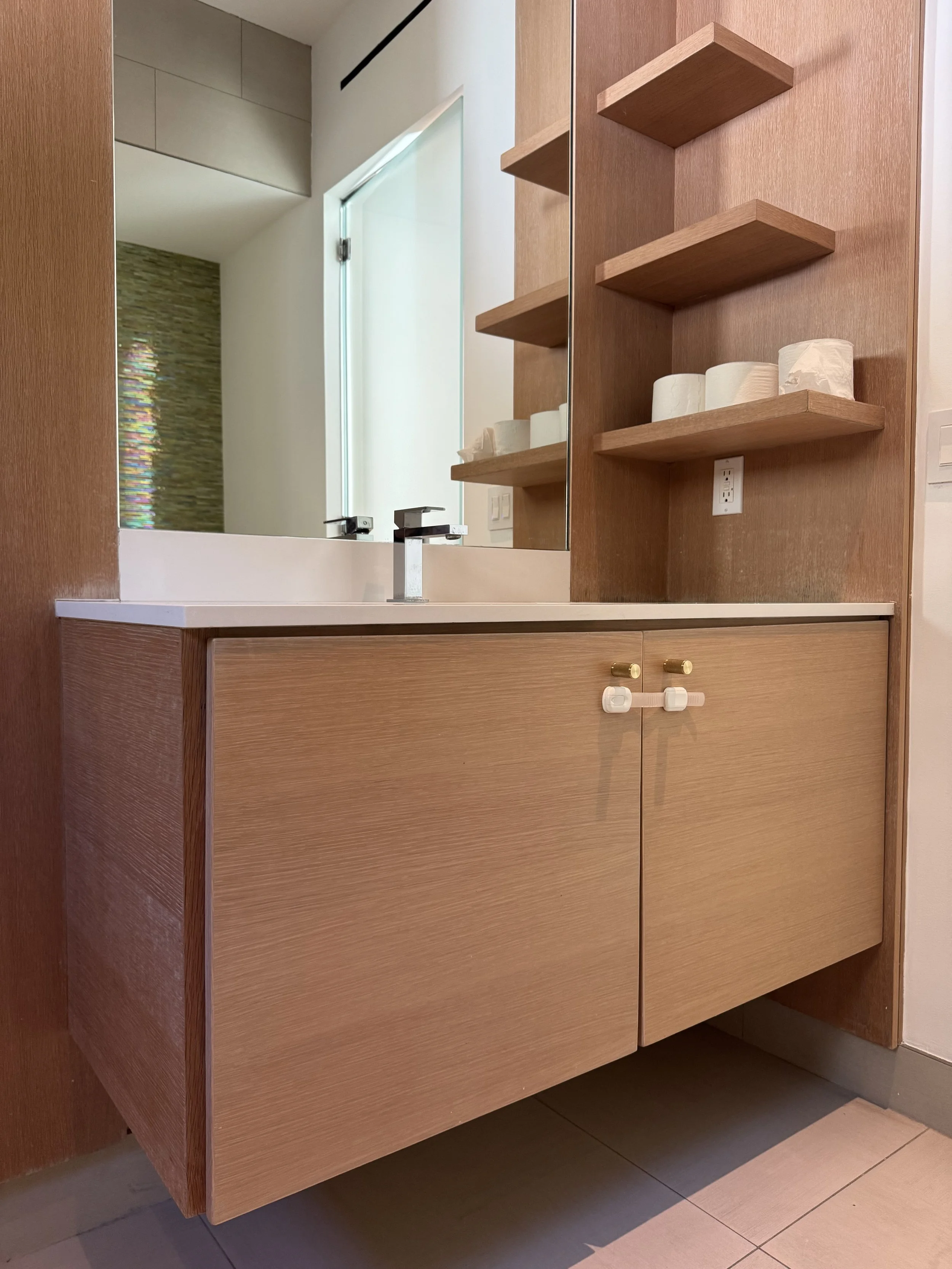 Bathroom sink with wooden cabinet, mirror, and open wooden shelves holding toilet paper rolls.