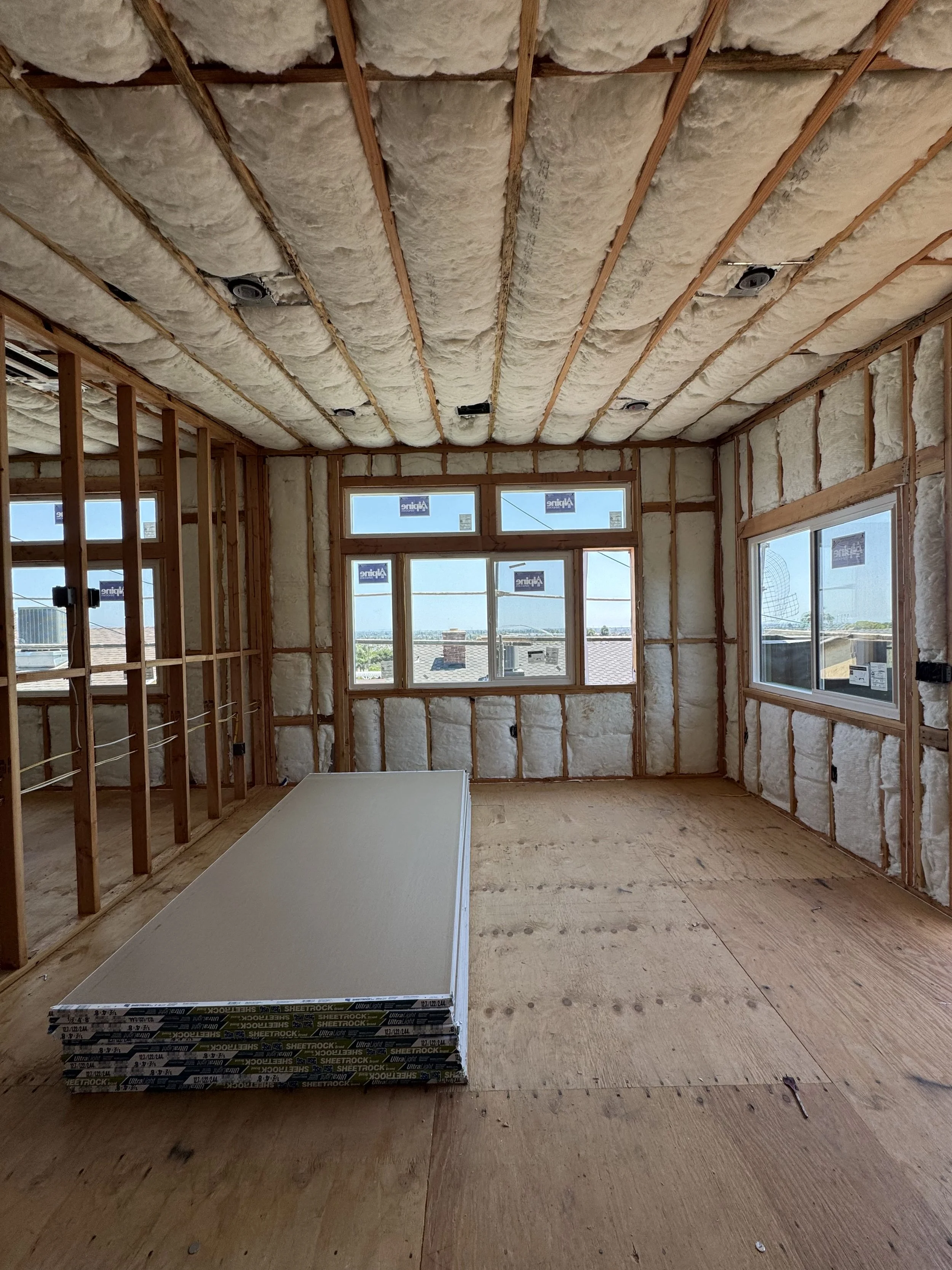 Unfinished room in a house under construction with insulation in the walls and ceiling, and multiple windows providing natural light.