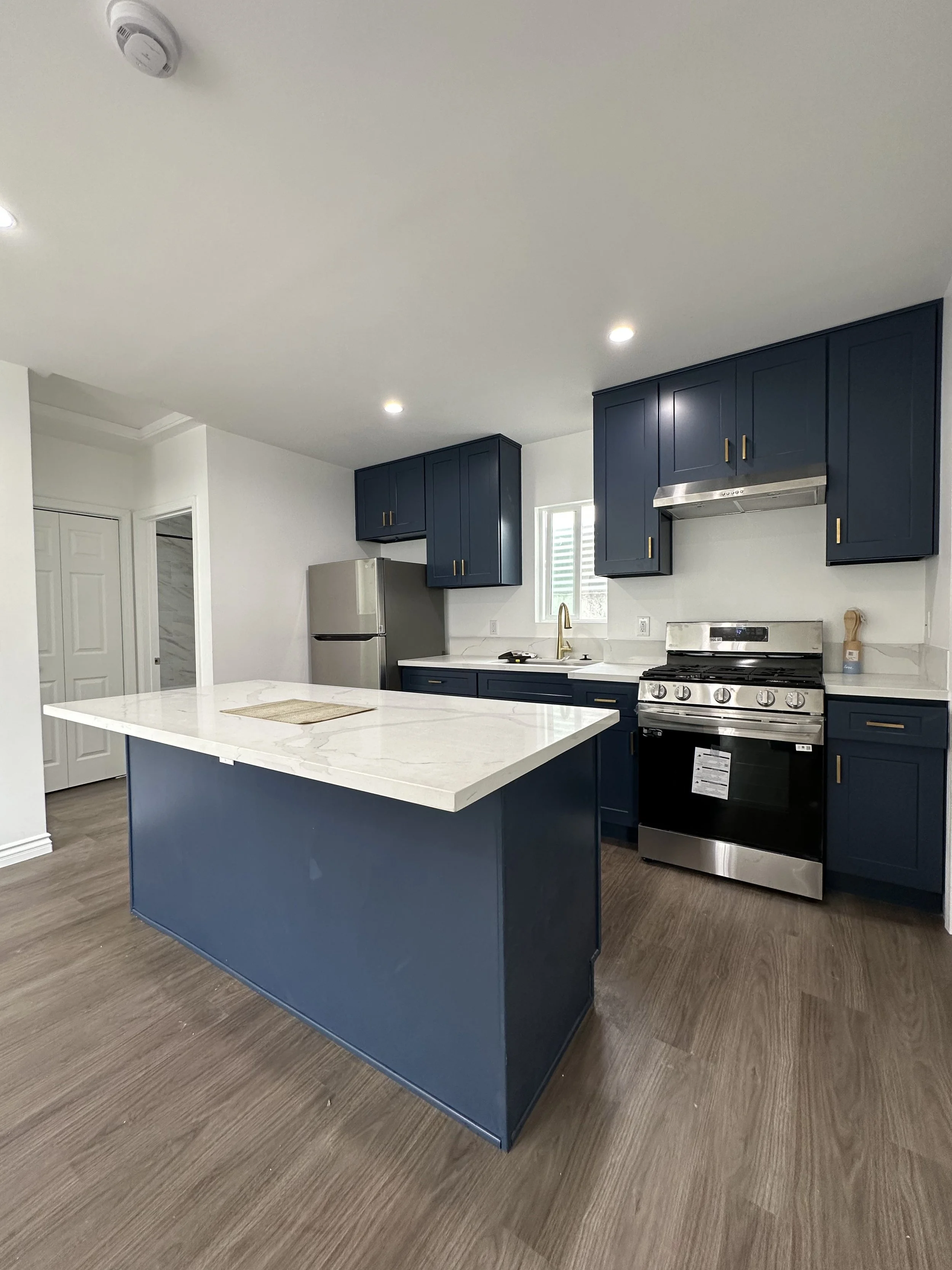 Modern kitchen with blue cabinetry, stainless steel appliances, white marble island, and wood flooring.
