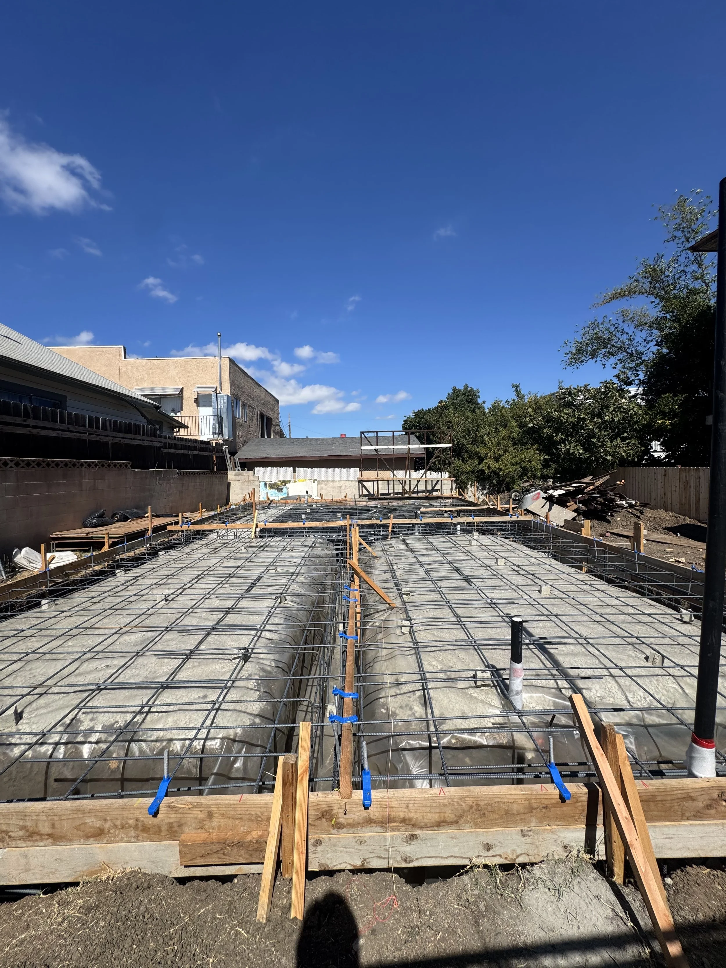 Construction site with rebar framework for concrete foundation, wooden forms, and a blue sky with some clouds.