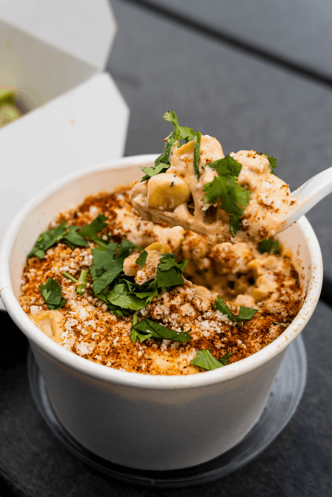 A bowl of cheesy dip topped with herbs and paprika, with a spoon lifting a portion.