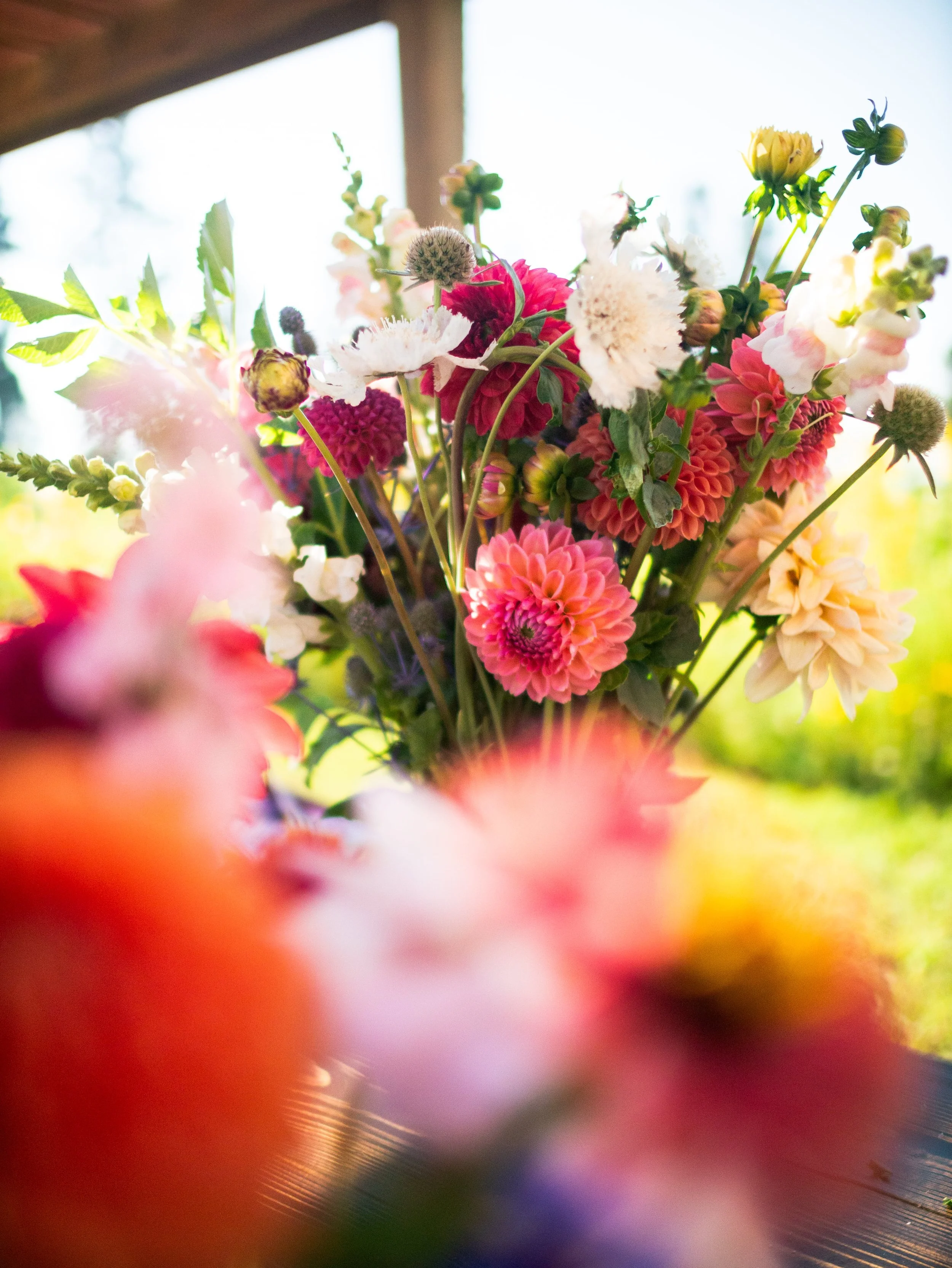 Colorful bouquet of pink, white, yellow, and purple flowers on a wooden surface with a blurred garden background.