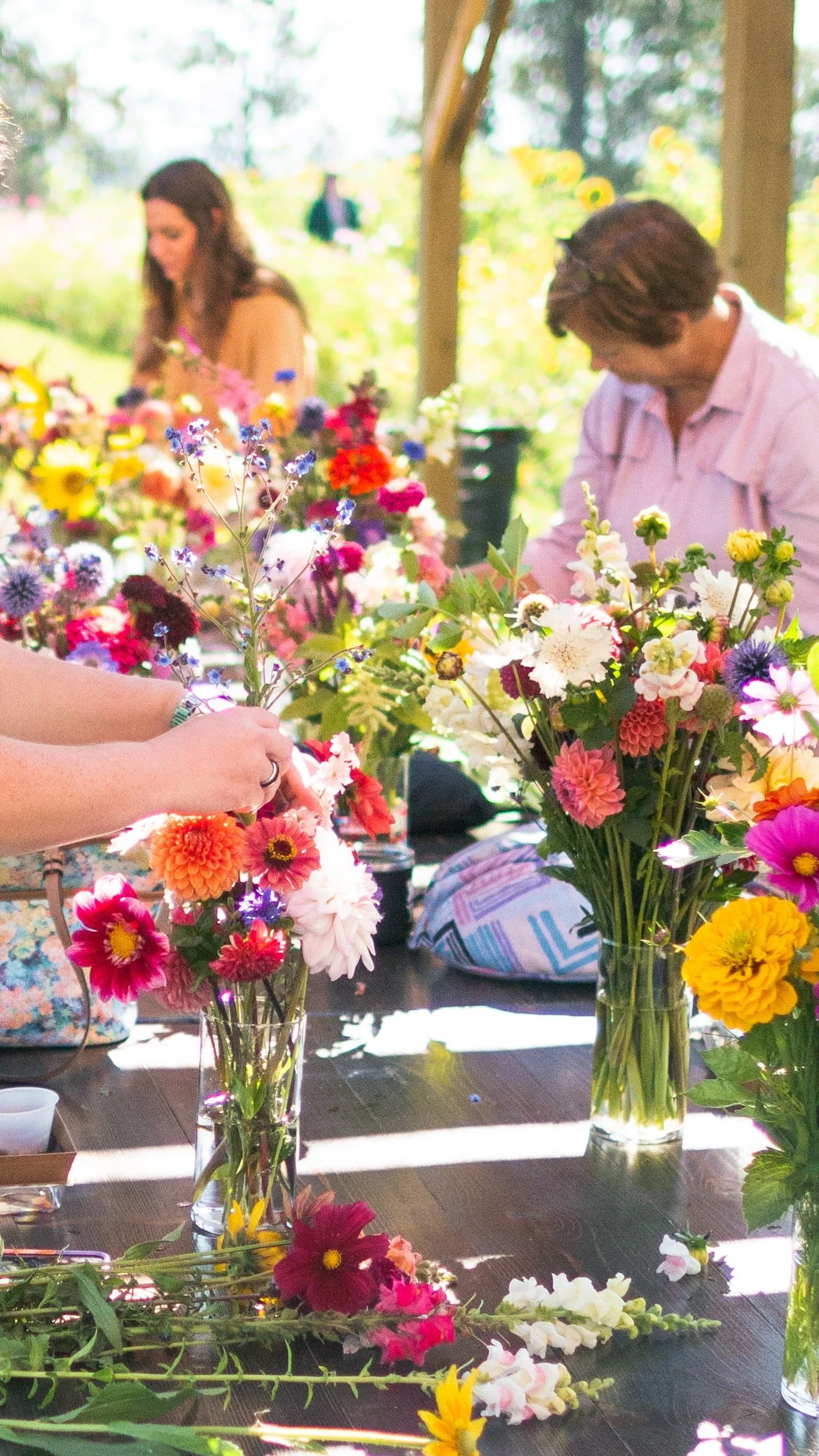 People arranging colorful flowers in vases outdoors on a sunny day