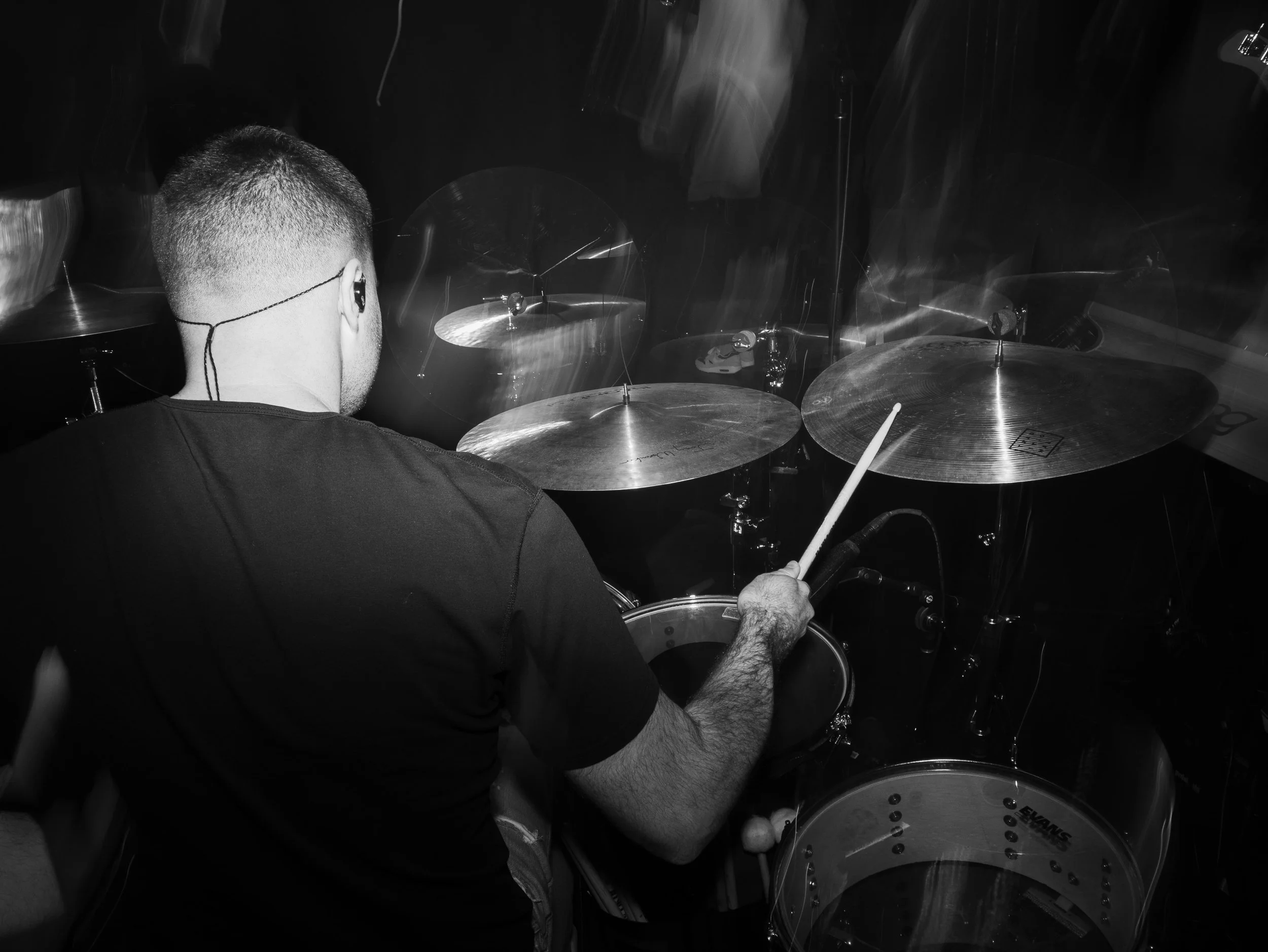 A musician playing a drum set in a dimly lit environment, with motion blur on cymbals.