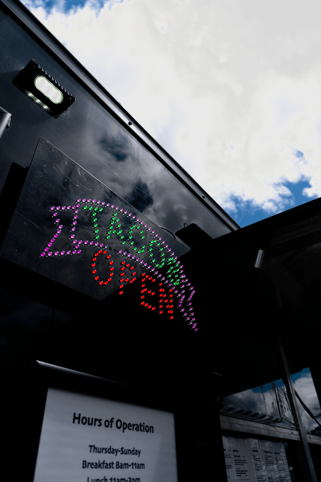 A neon sign reading 'Z Top Shop' mounted on the exterior of a food truck with a reflective black surface against a partly cloudy sky.