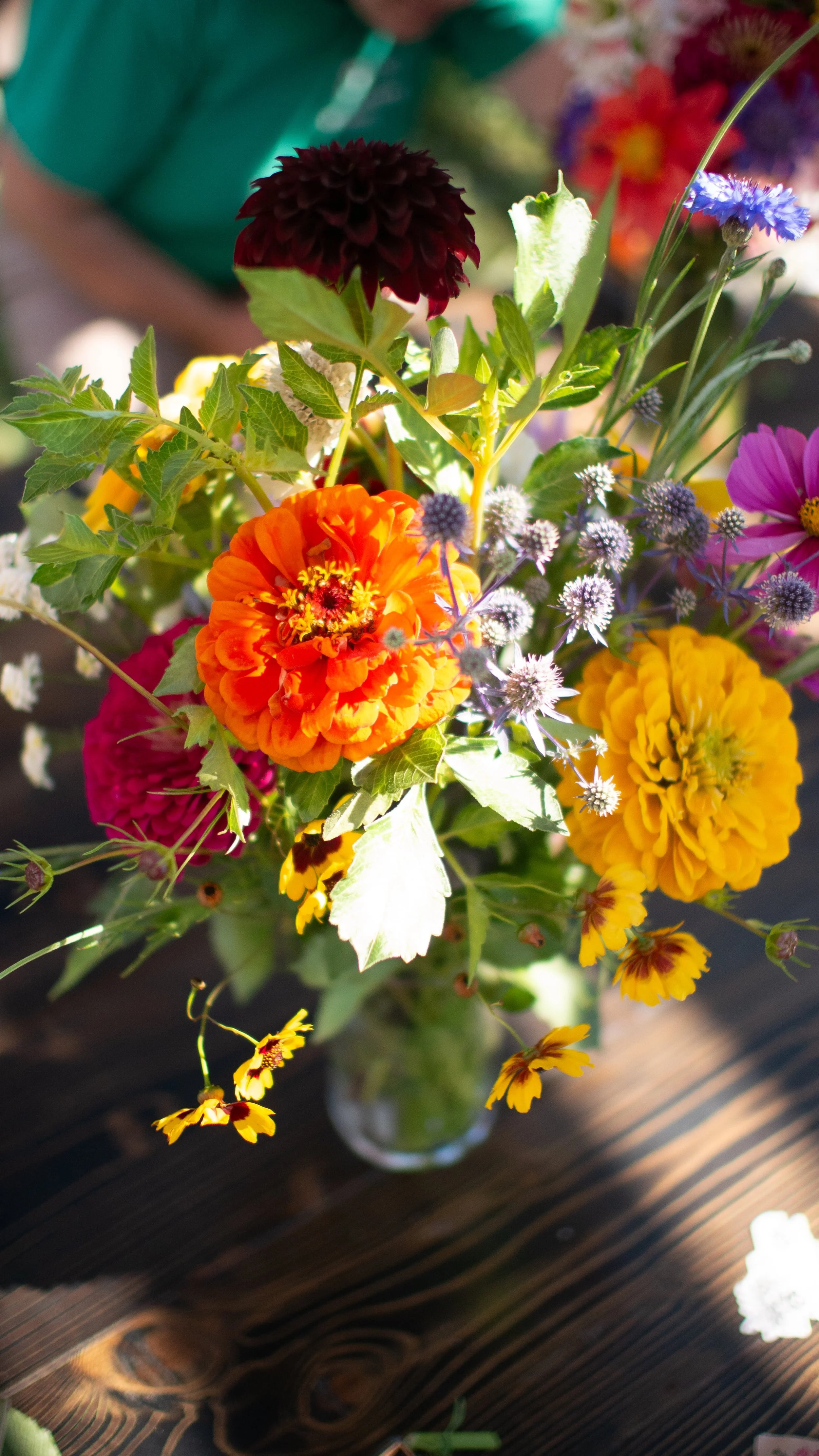 Colorful bouquet of various flowers in a glass vase on a wooden surface.