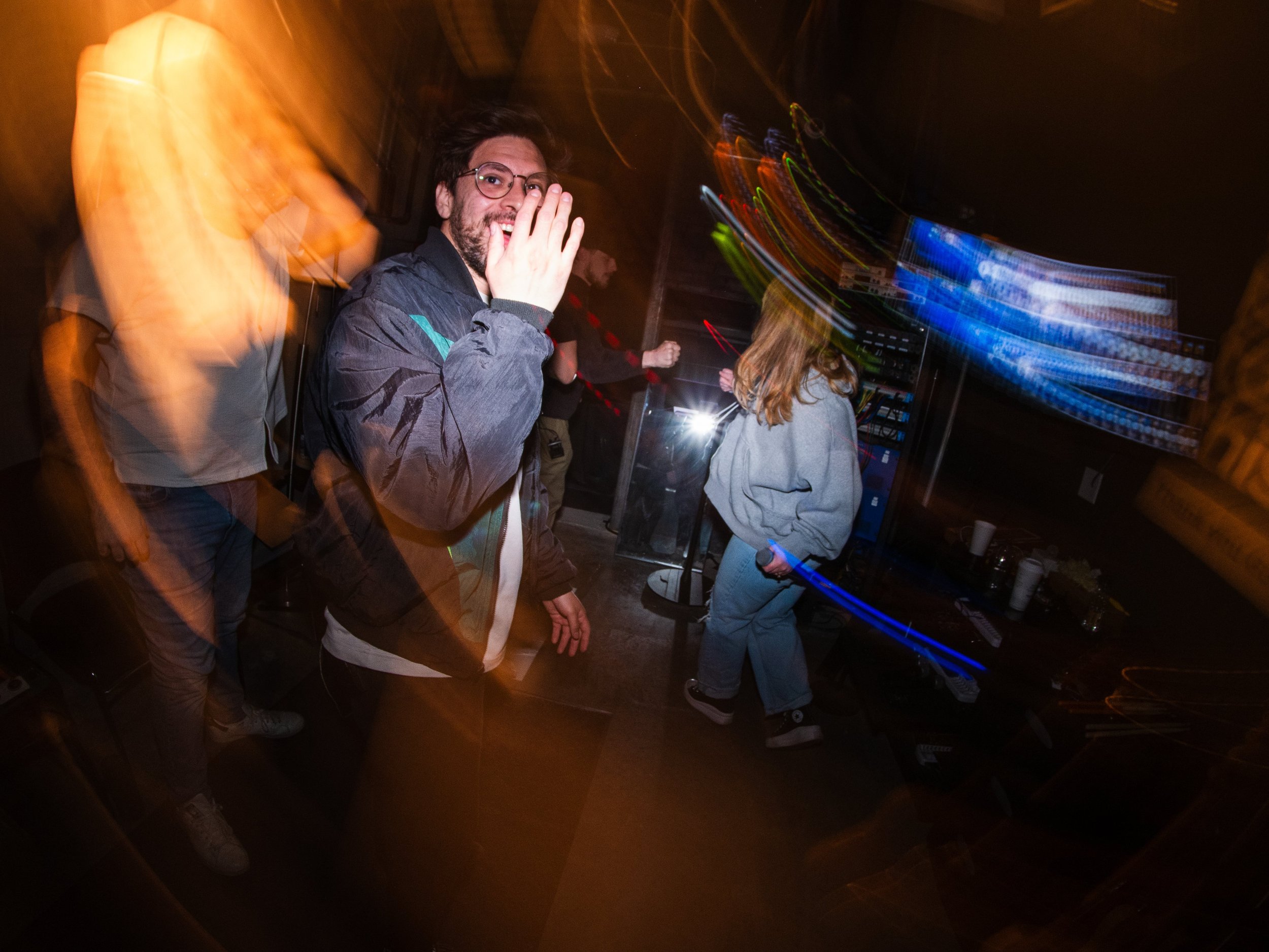 People dancing at a party with colorful lights and a DJ booth.