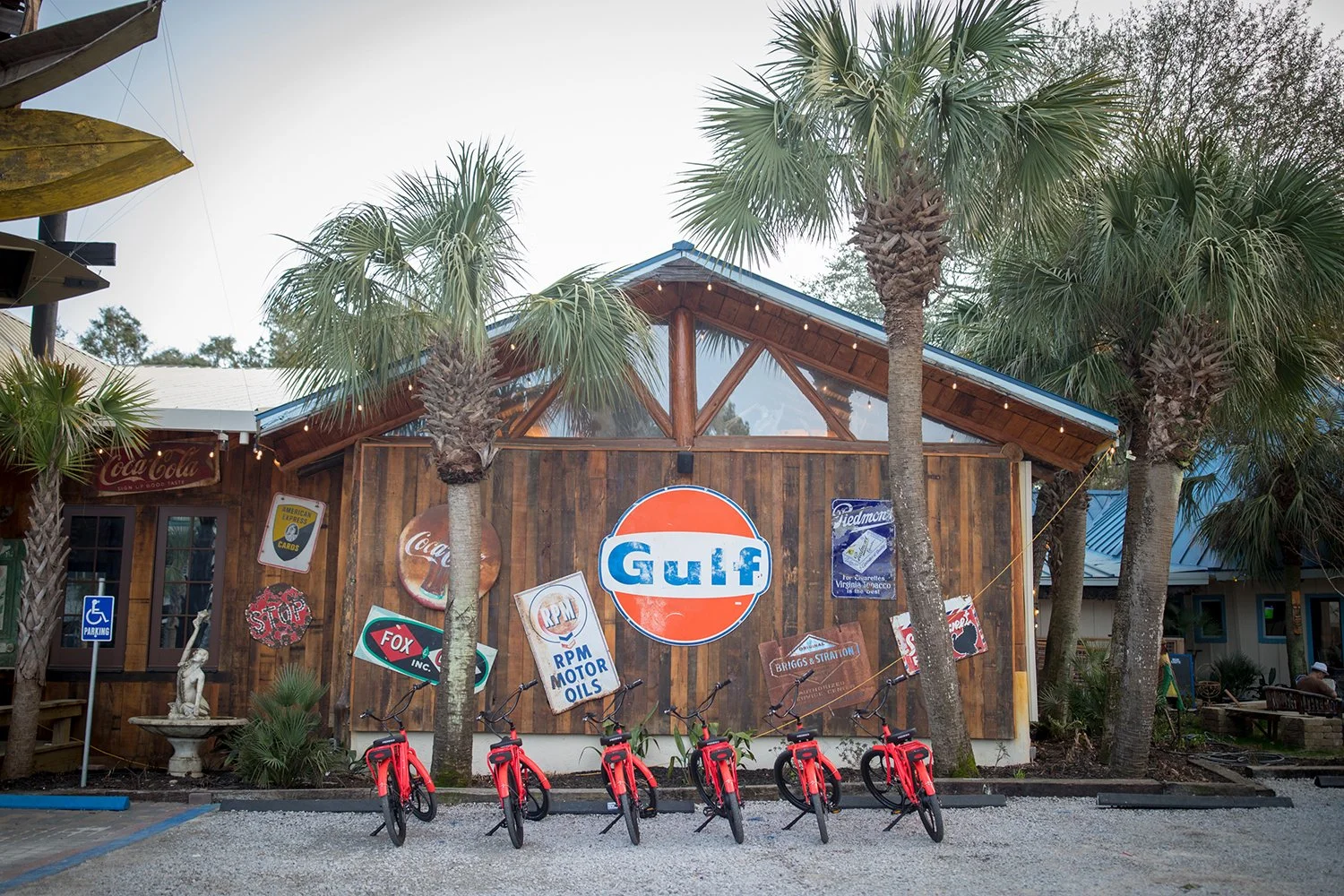 Wooden building with vintage Gulf and Coca-Cola signs, palm trees, and red bicycles parked in front.