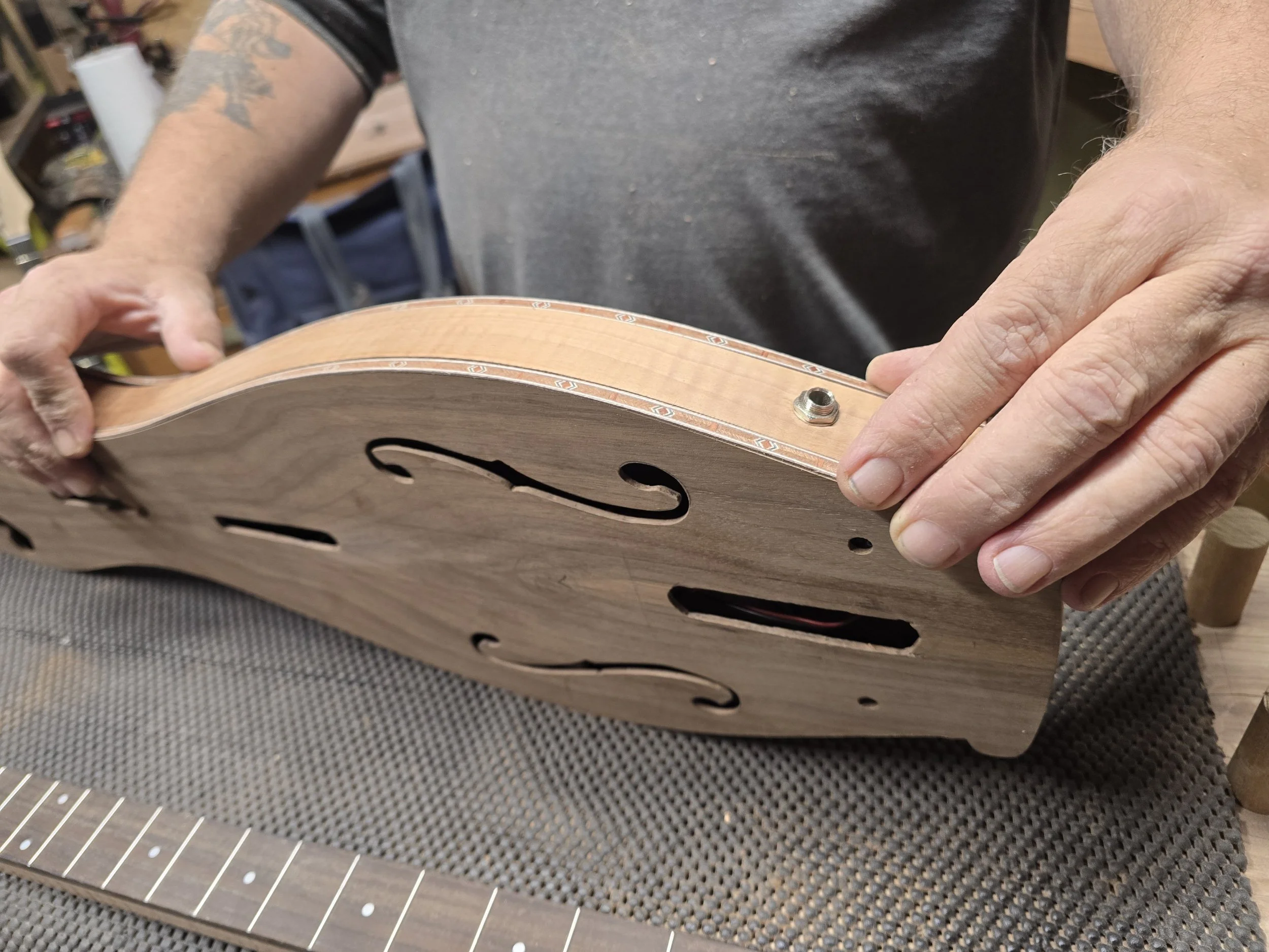 Close-up of person assembling a guitar body, with parts of the guitar neck visible, in a woodworking workspace