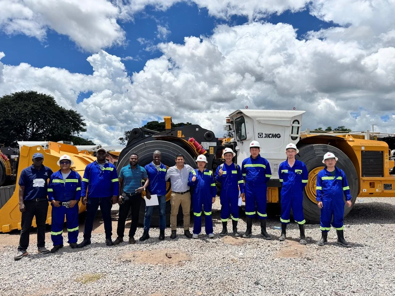 Grupo de trabajadores con casco en una construcción con maquinaria pesada al fondo y cielo con nubes.