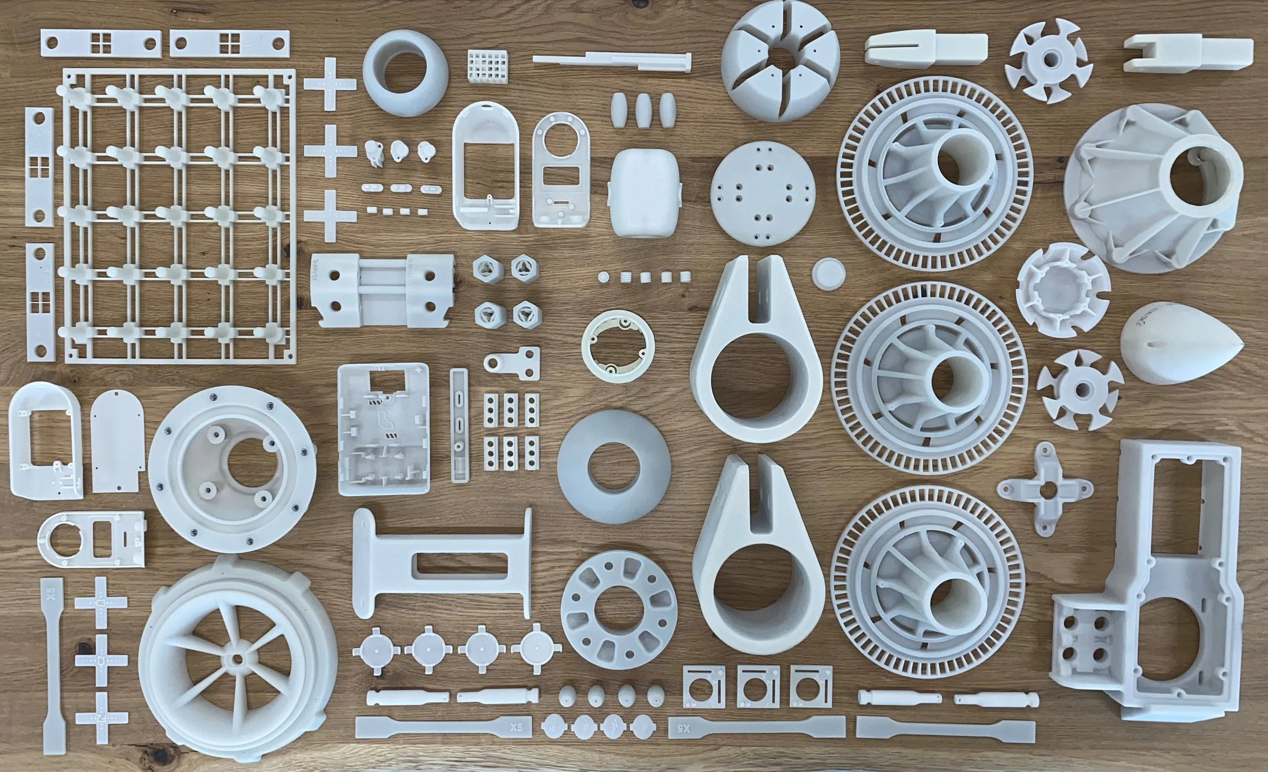 Various white plastic parts and components laid out on a wooden surface, likely parts for a mechanical or electronic assembly or device.