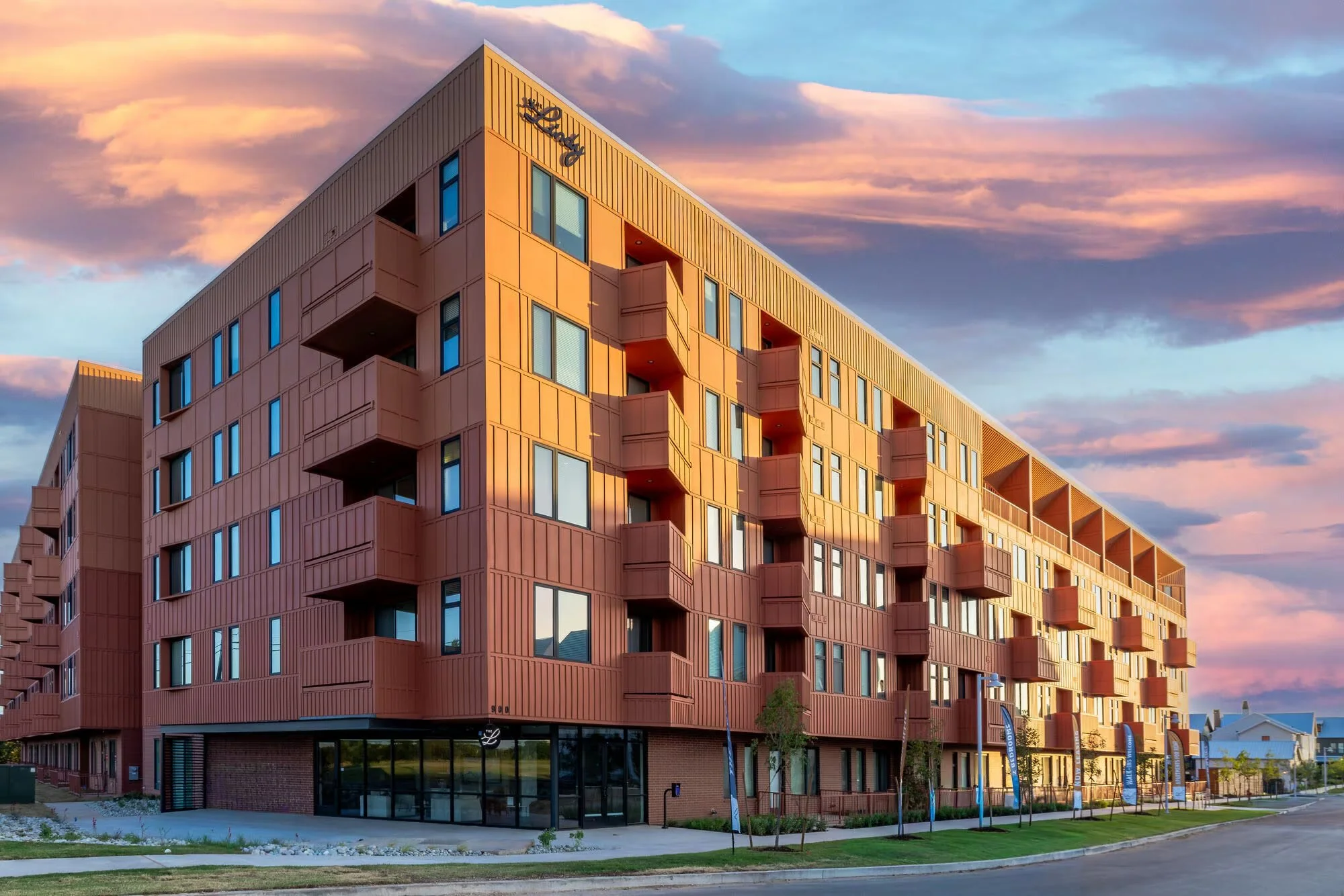 The Lindy apartments in Oklahoma City, showing the red-earth facade and balconies at dusk.