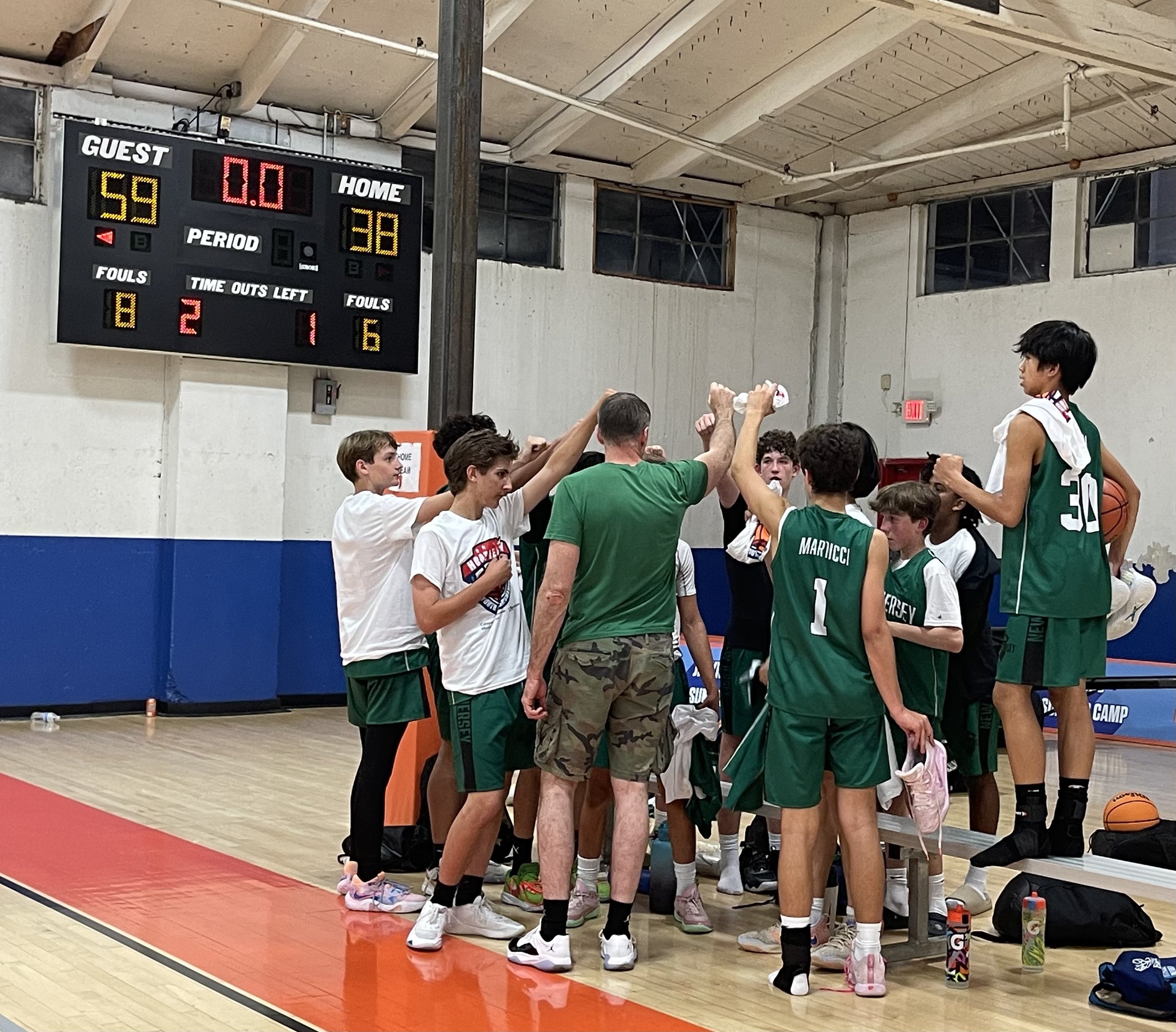 Youth basketball team and coach celebrating during a timeout in a gymnasium.
